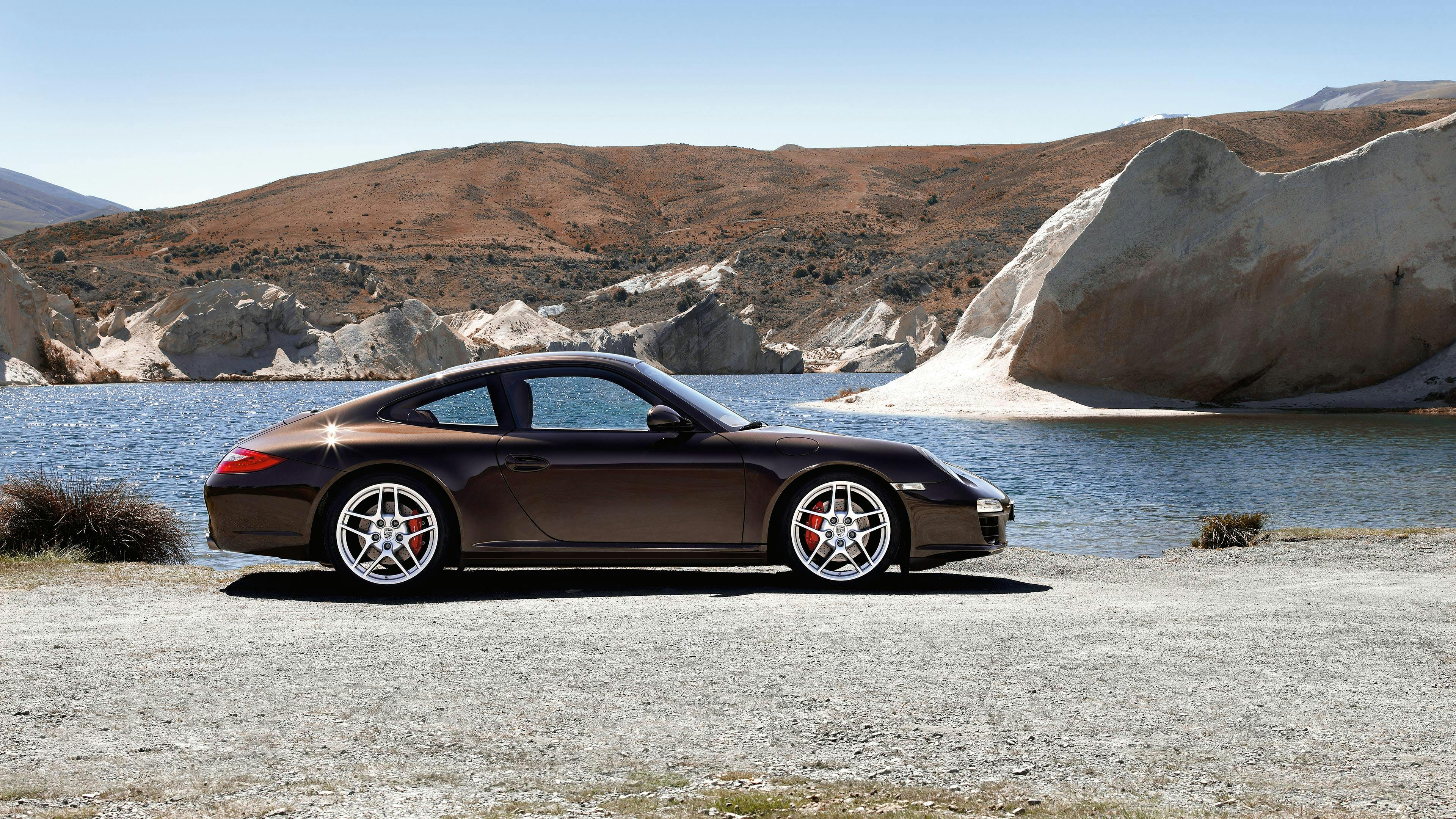Parked brown 997 911 Carrera Coupé on a lakeshore.