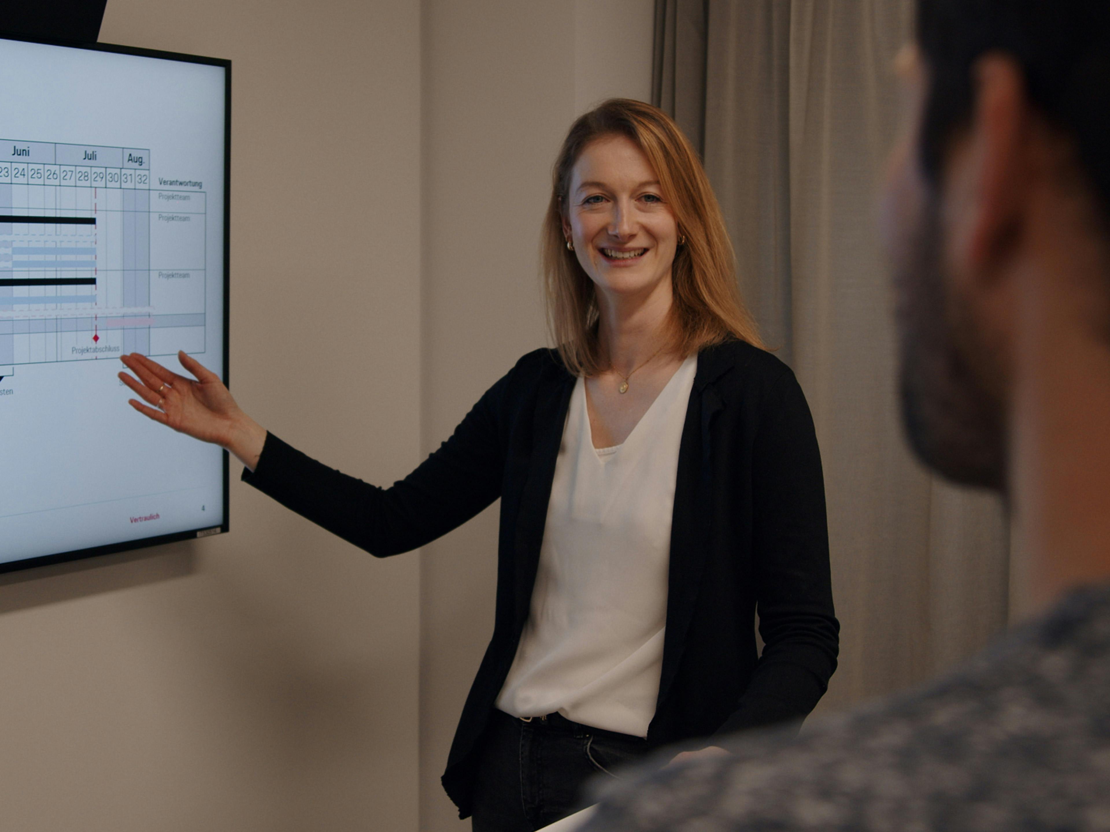 Die Porsche Mitarbeitern Vivien zeigt einem Kollegen eine Auswertung an einem digitalen Monitor.