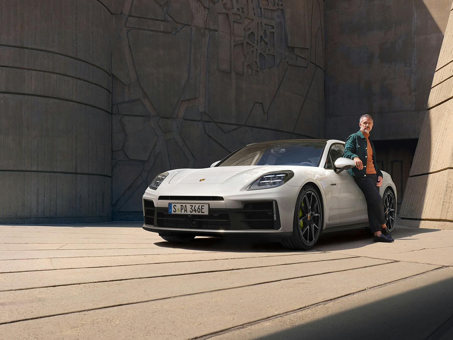 Weißer Porsche Panamera steht auf einem gepflasterten Platz, eine Person lehnt an der Fahrerseite.
