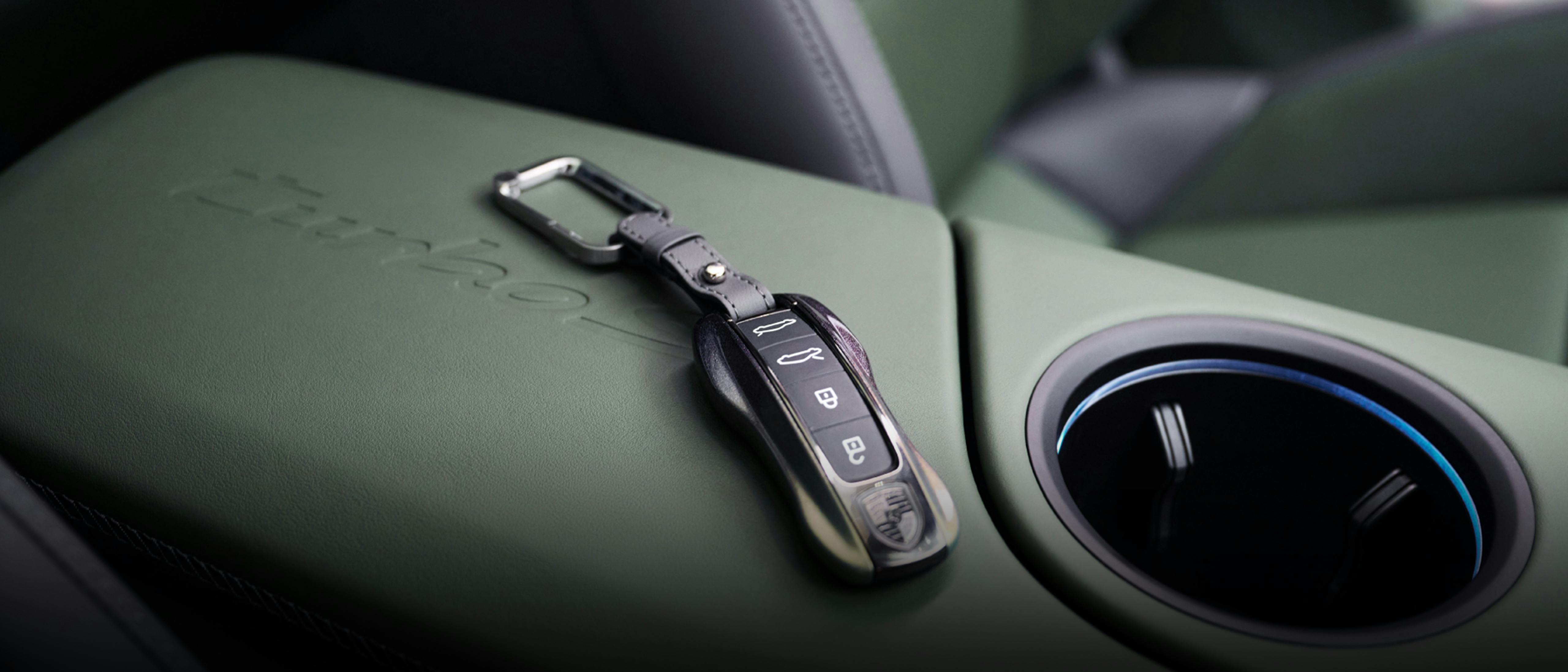 A close-up of a Porsche car interior featuring a green leather console with embossed branding, a stylish key fob, and a cup holder with blue lighting accents.