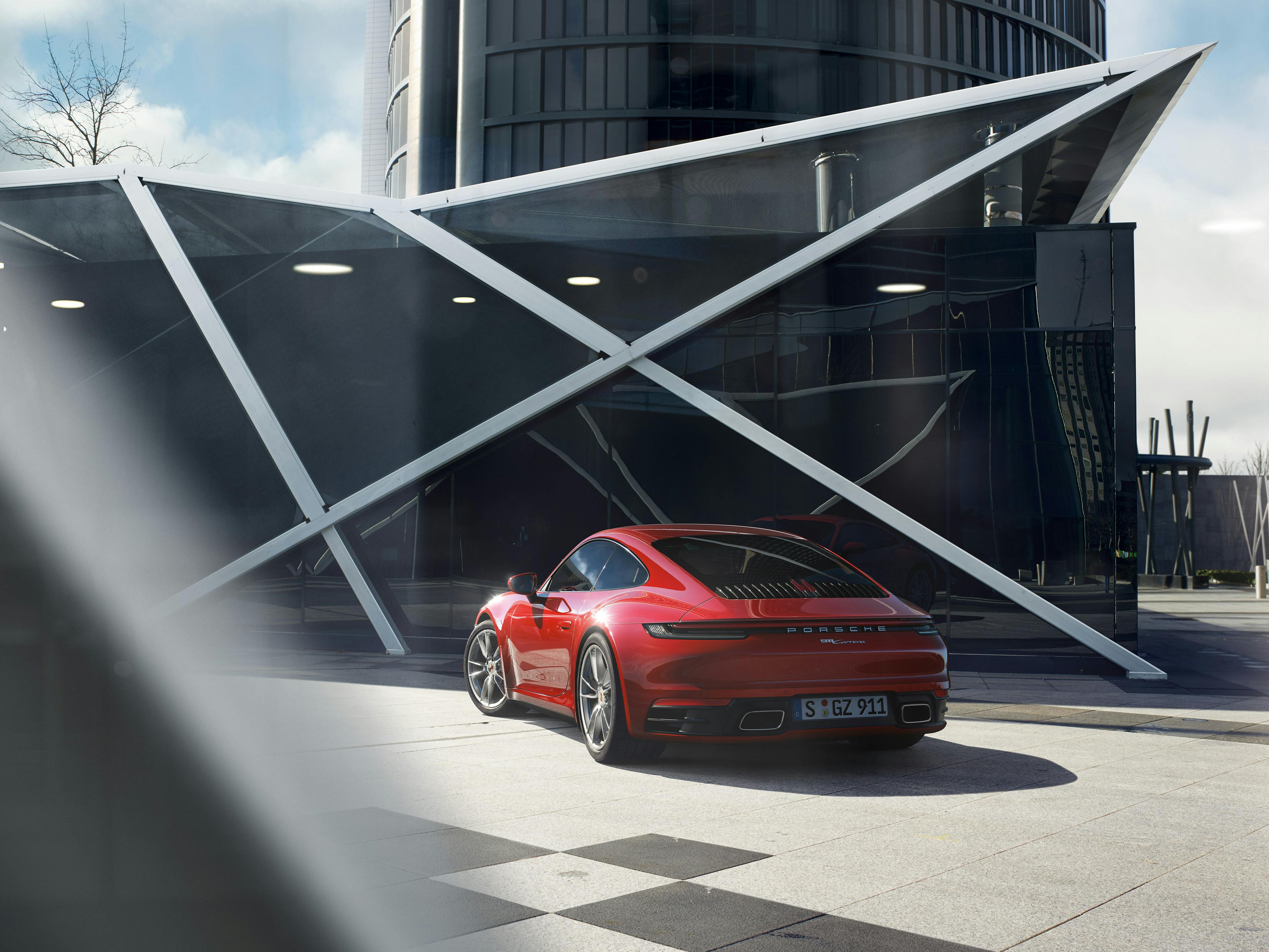 Une Porsche 911 Carrera rouge garée devant un impressionnant bâtiment moderne.