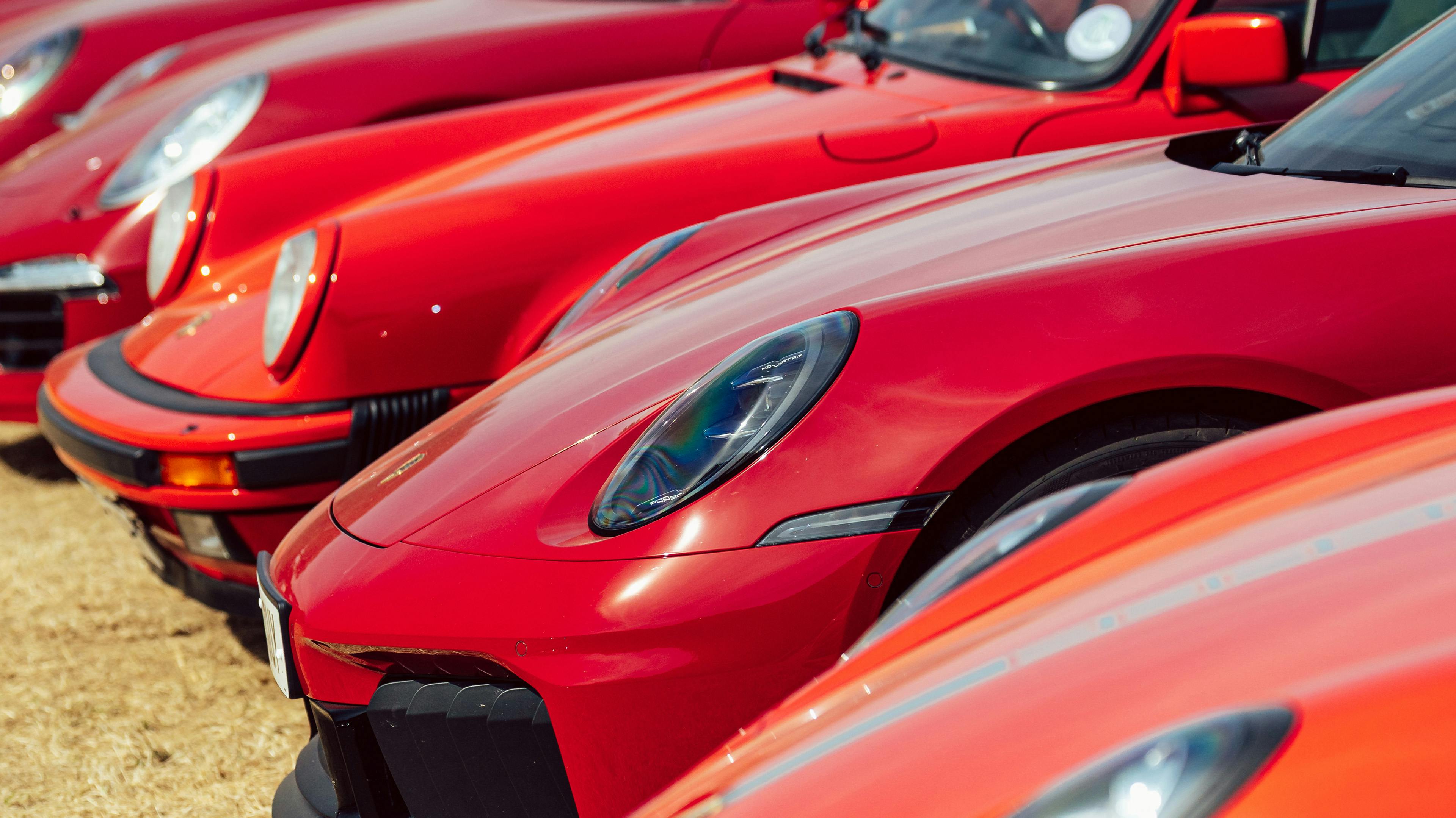 Close-up of a row of red Porsche 911s parked side by side, front ends and headlights in focus.