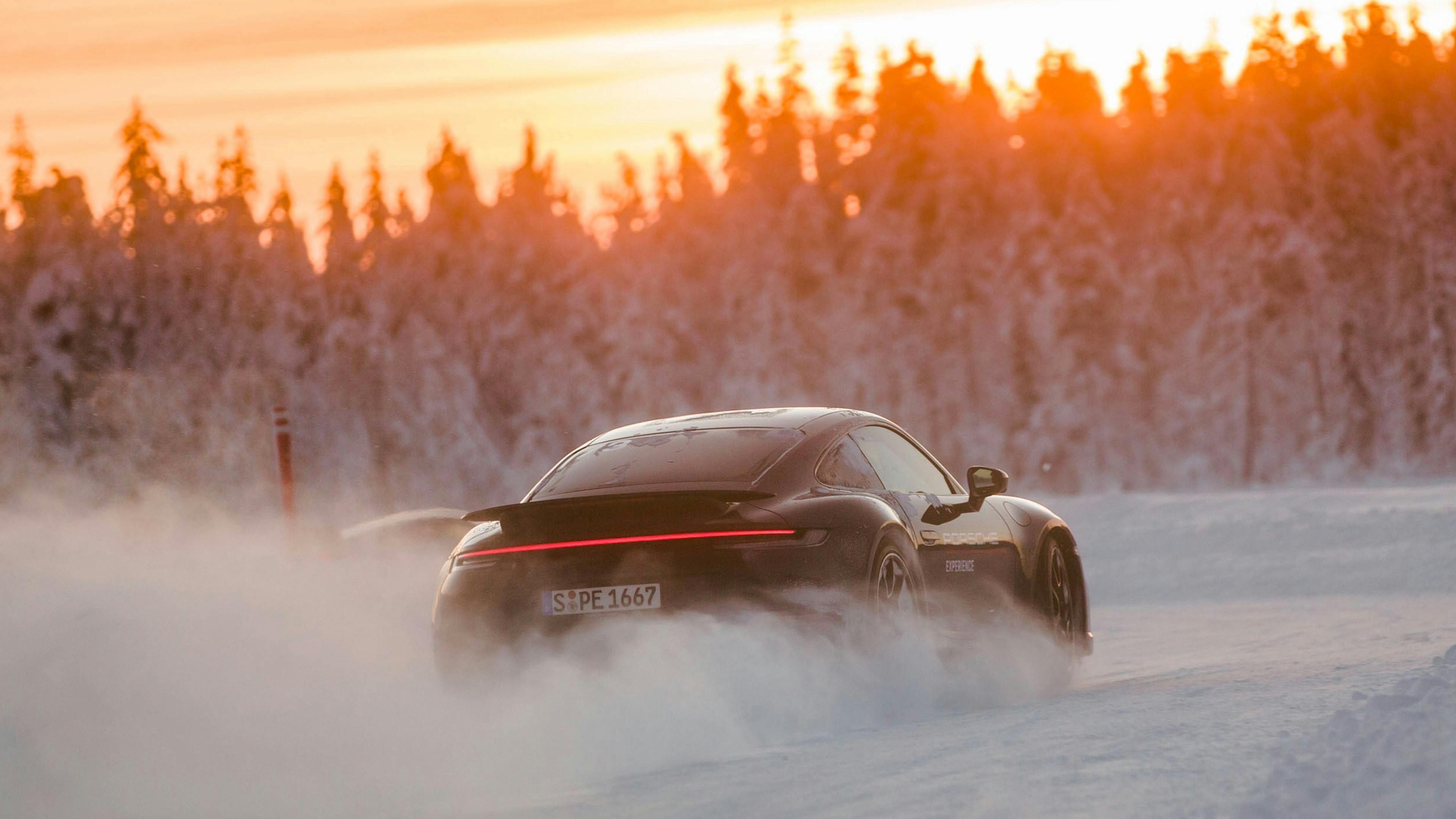 A Porsche car driving along a snow-covered road at sunset.