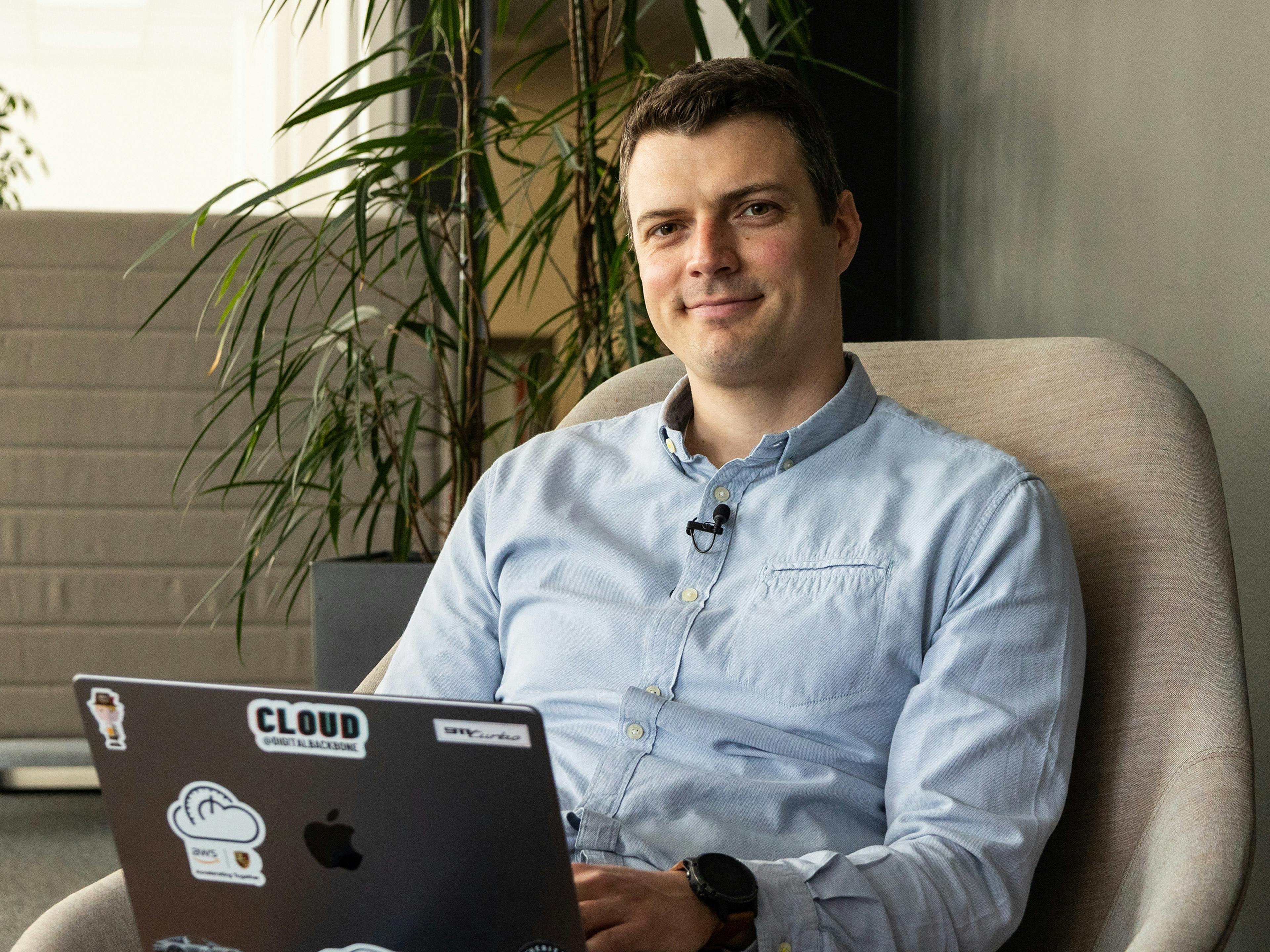 Der Porsche Mitarbeiter Philipp sitzt auf einem gemütlichen Stuhl am Laptop und lächelt in die Kamrea.
