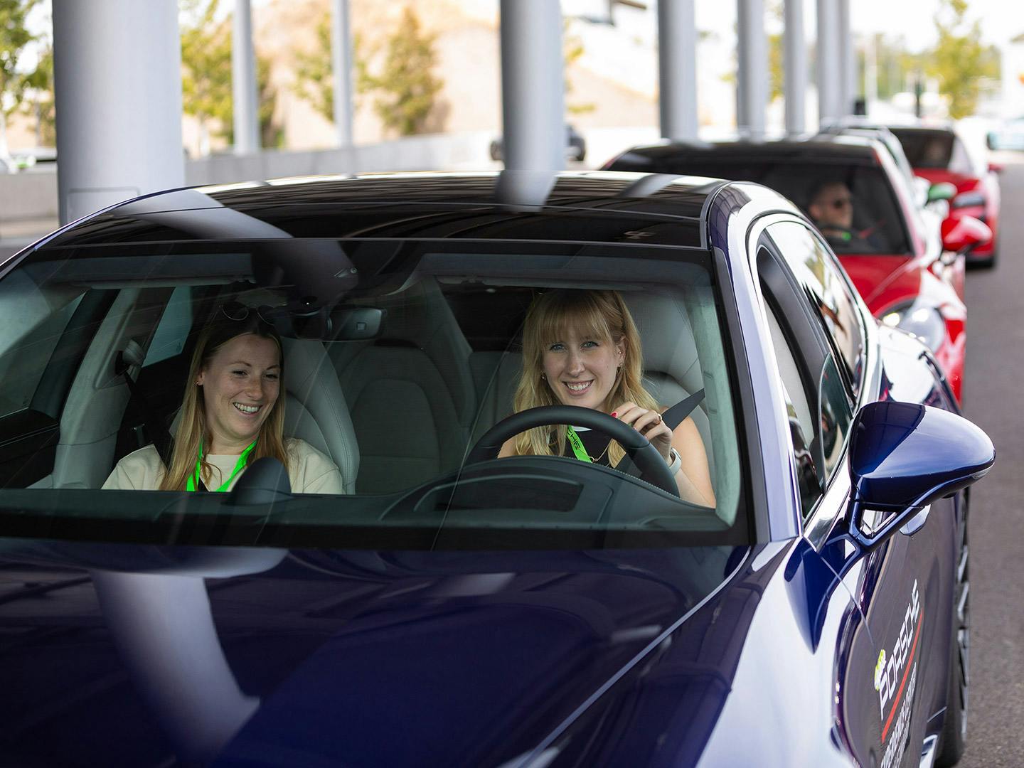 Eine Reihe von Autos in verschiedenen Farben, im Vordergrund ein Porsche in dem zwei Frauen sitzen.