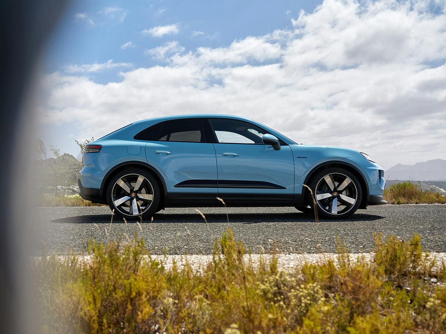 Vue latérale d'une Porsche Macan bleue sur une route côtière.
