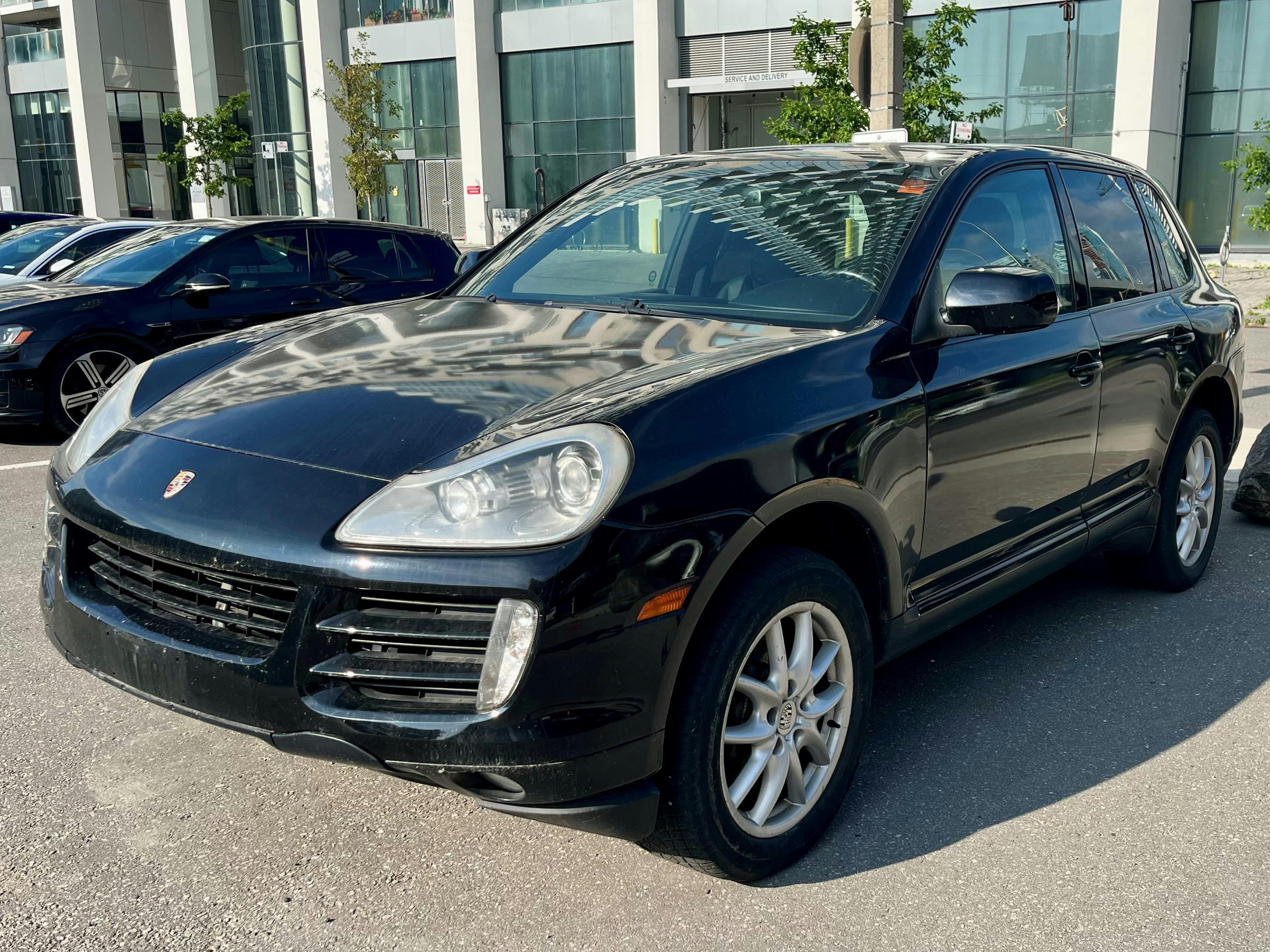 A front shot of a black first-generation Porsche Cayenne in a parking lot.