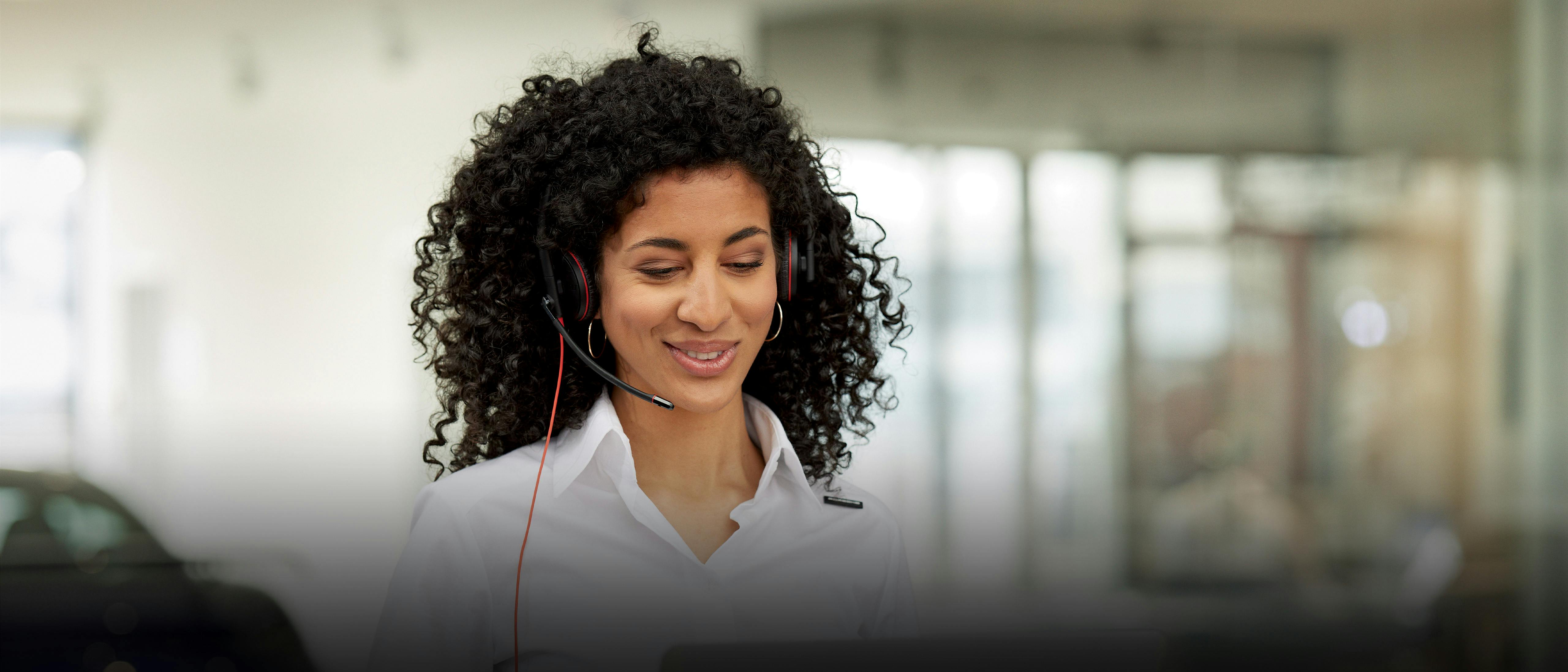 A Porsche service assistant is in a conversation via headphones and looking at her laptop.