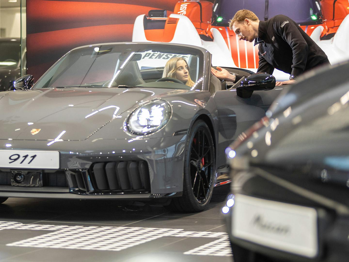 Un employé de Porsche assis derrière un bureau dans une salle de réunion montre à un collègue masculin quelque chose dans un catalogue posé sur le bureau entre eux.