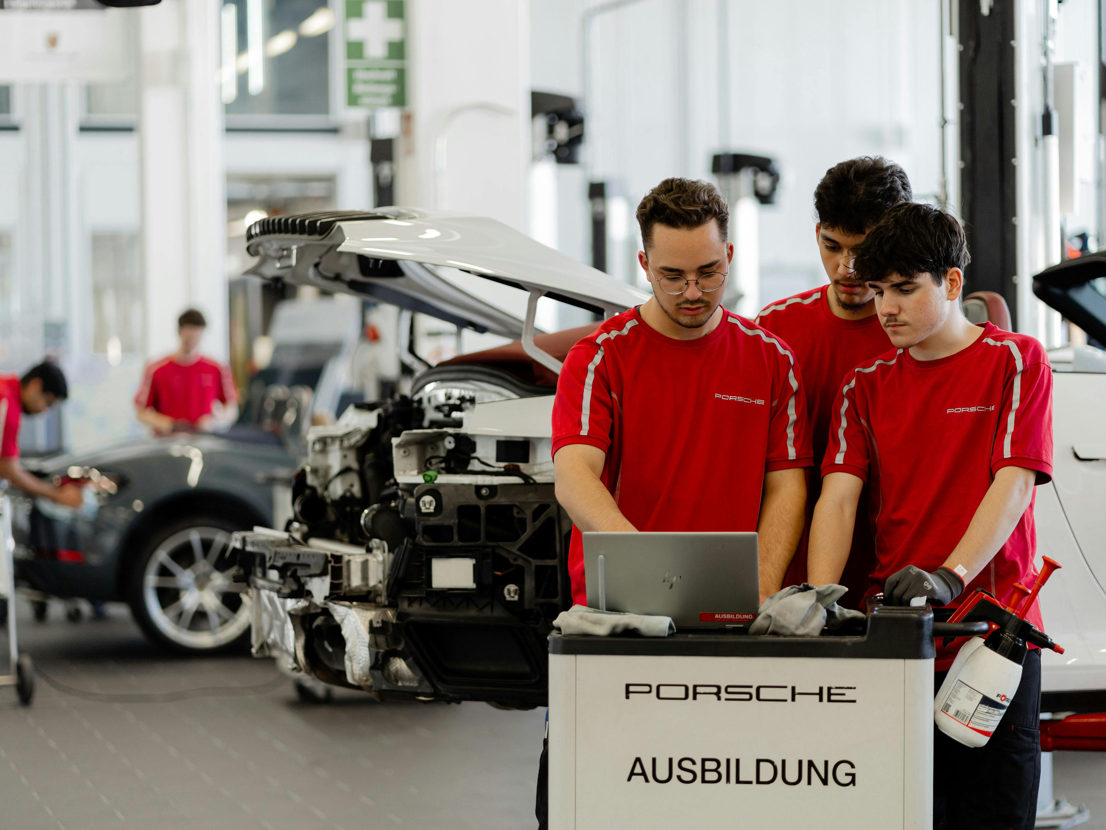 Drei Auszubildende diagnostizieren gemeinsam in einen Laptop ein Fahrzeug in der Ausbildungswerkstatt.