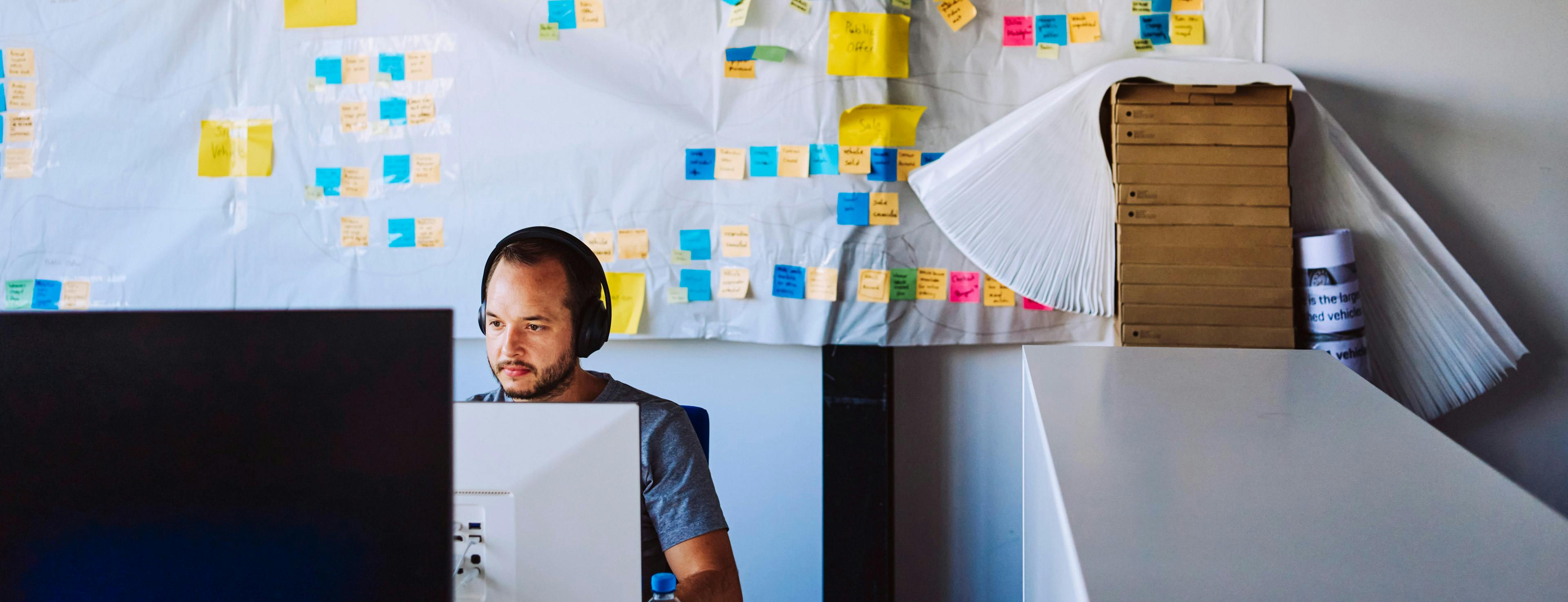 A Porsche employee is sitting in front of a monitor, with colourful sticky notes stuck to the wall in the background.
