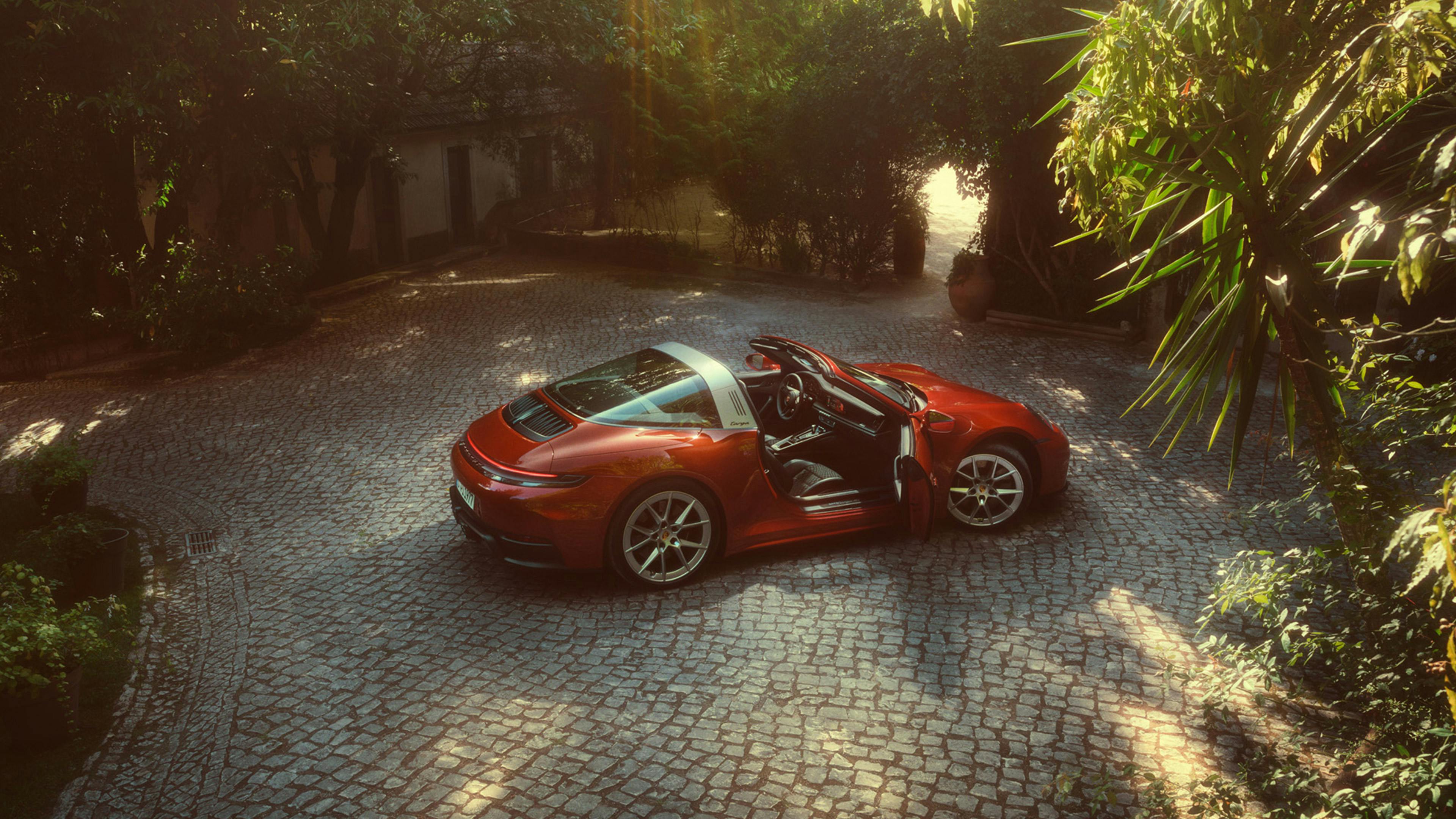 911 Targa with Heritage Design Package Pascha stands on a paved surface, driver's door open, sunlight shining through the trees.