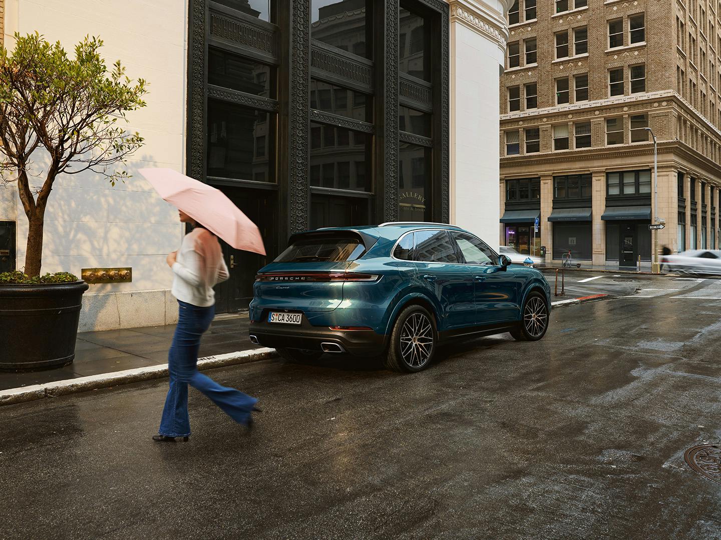 Vrouw loopt in de regen met een paraplu voor de Porsche Cayenne.