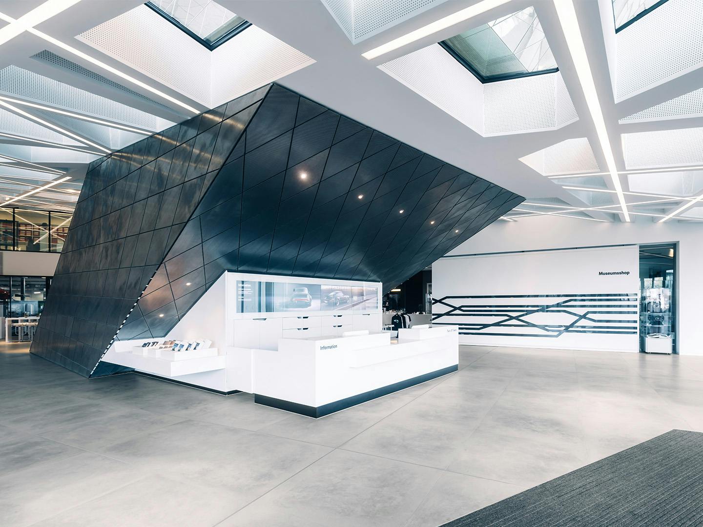 Open entrance area of the Porsche Museum with a striking black angular architectural structure and white information desk