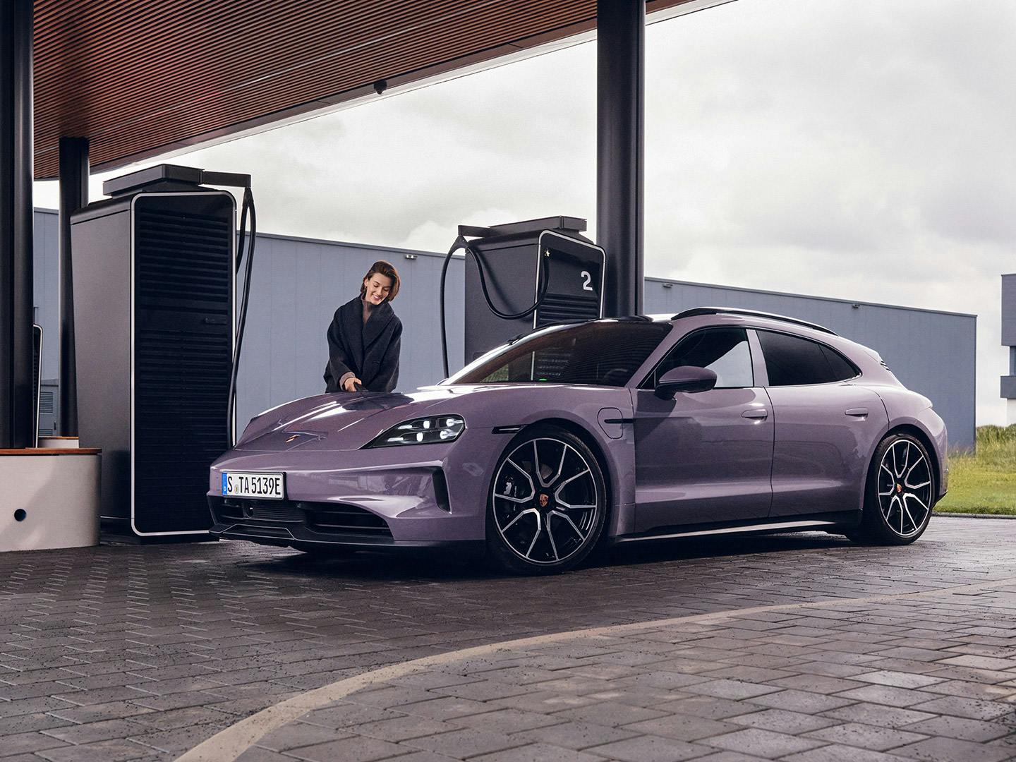Une dame est en train de brancher son Porsche Taycan à une station de recharge Porsche.
