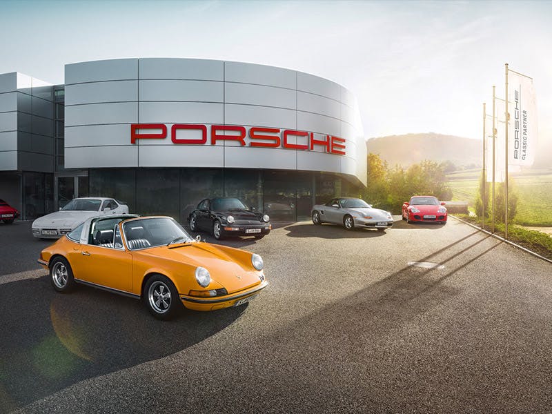 Porsche Classic Partner, Red logo on the building, various Porsche models in the front car park.