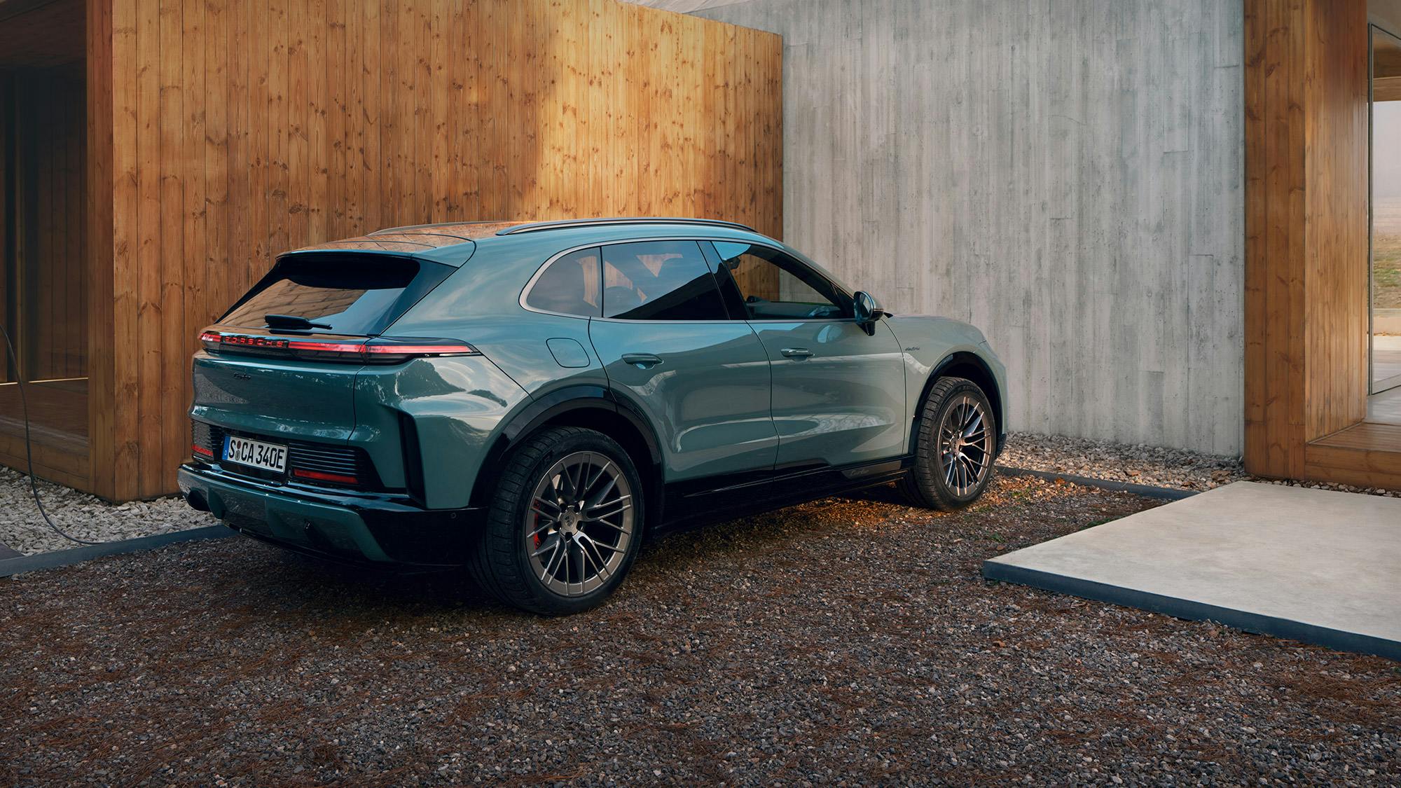 A Porsche Cayenne Turbo is charging at a Porsche Wallbox in front of a building made of concrete and wood.