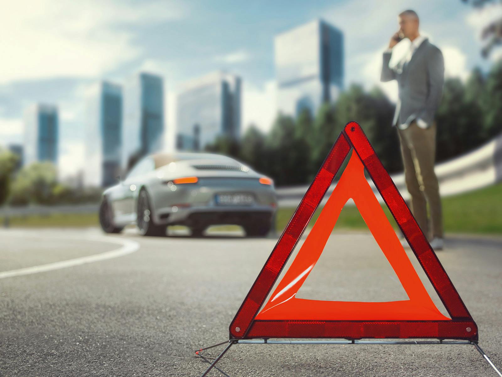 Ein Mann telefoniert mit einem roten dreieckigen Straßenschild im Vordergrund und einem Porsche im Hintergrund in einer städtischen Umgebung.