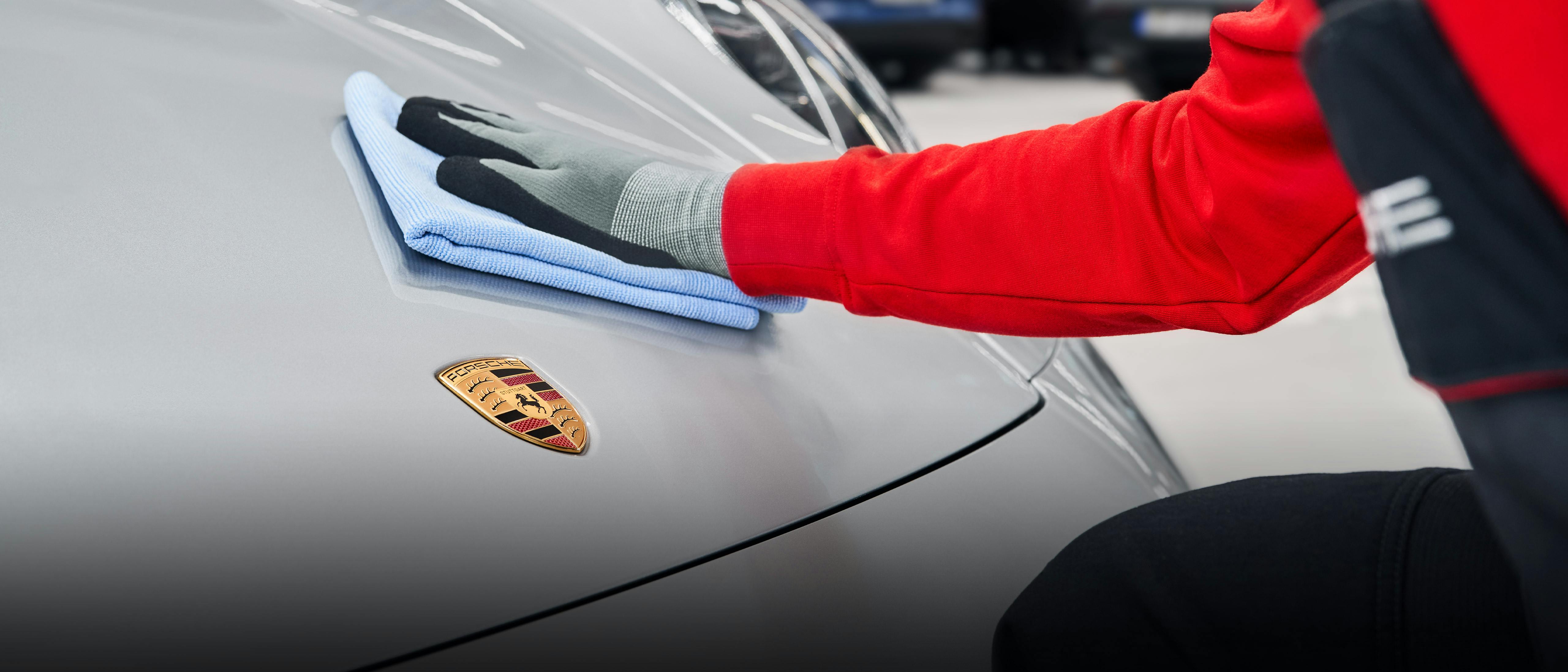 A close-up of a member of the workshop wiping down a Porsche 911 with a cloth.