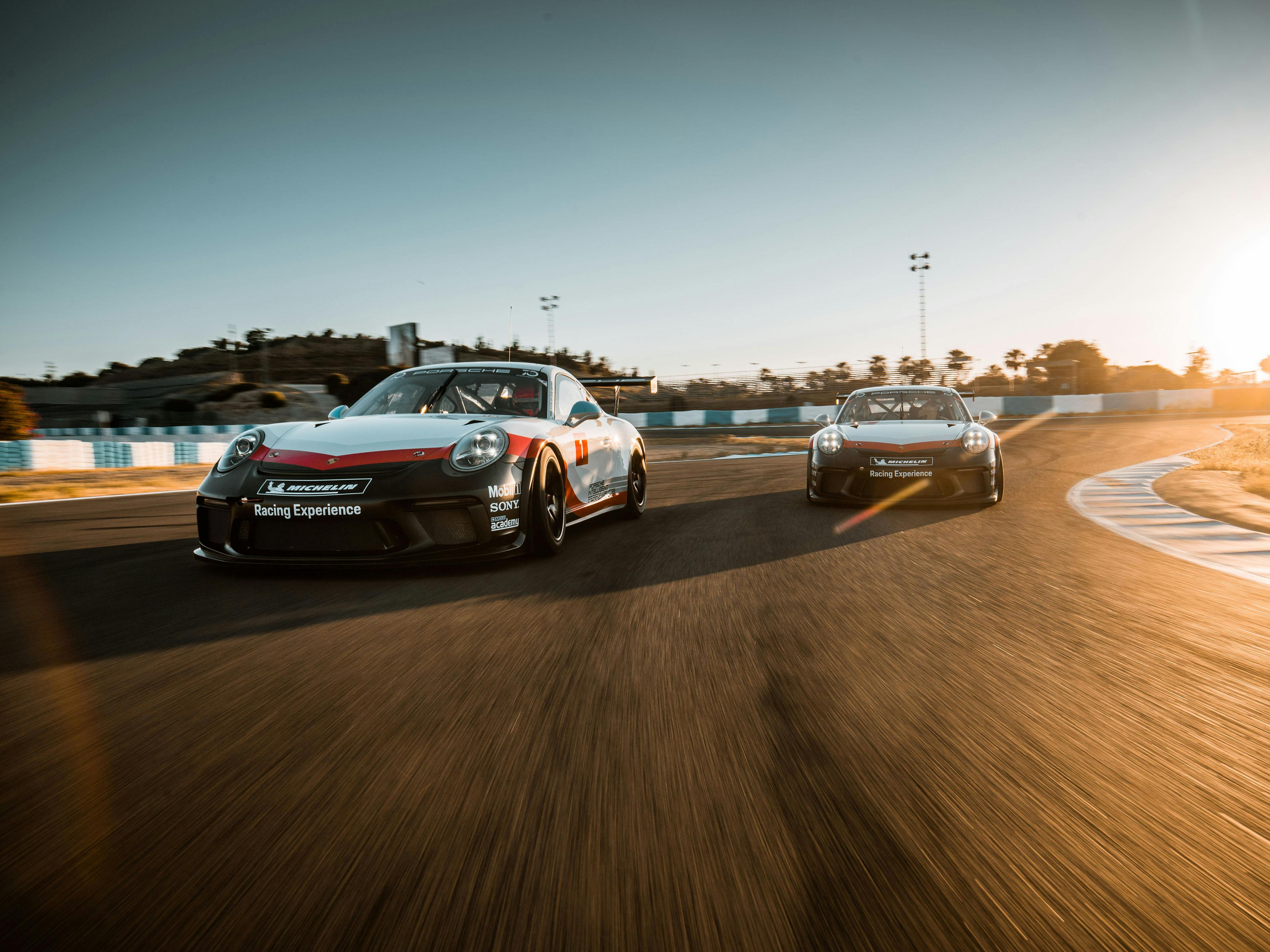 Zwei Porsche 911 RSR auf der Rennstrecke bei Sonnenlicht.