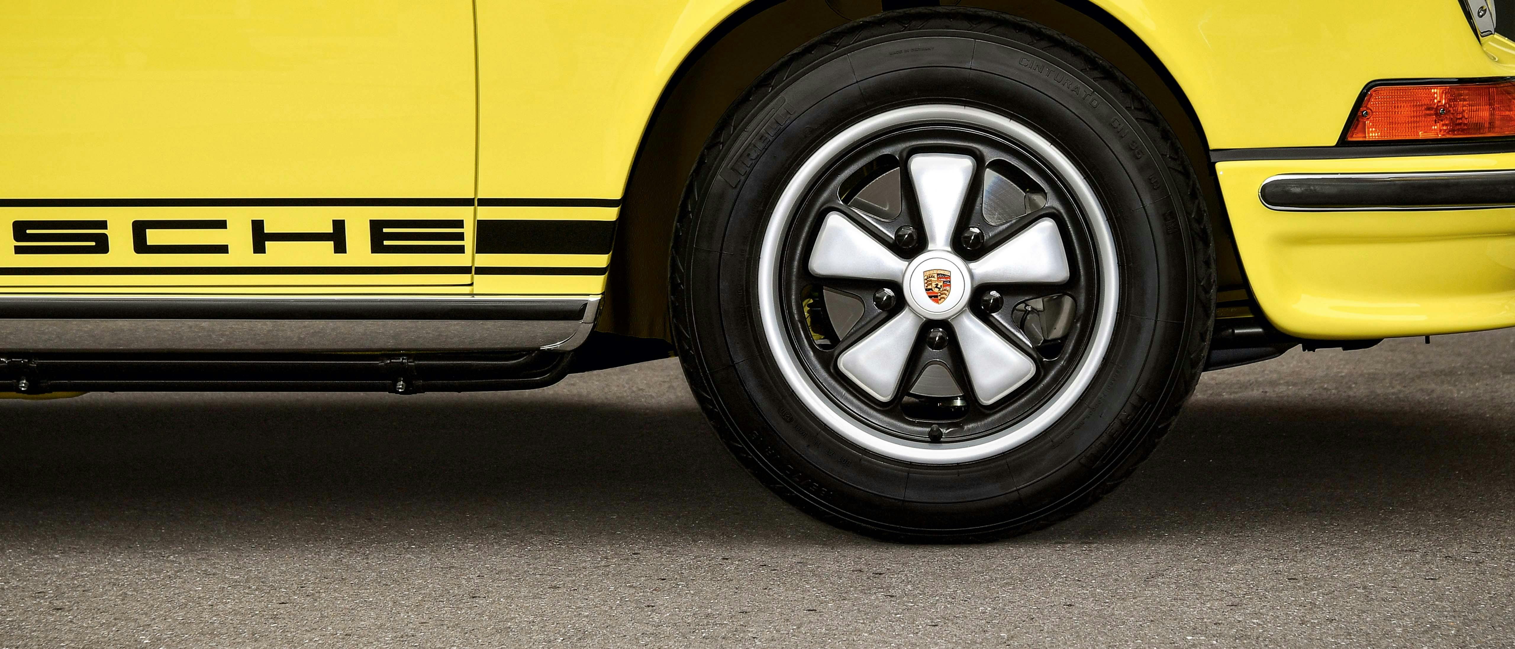Vista laterale della parte anteriore di un classico giallo con pneumatici neri, coprimozzo decorativi argentati, paraurti e scritta Porsche laterale.