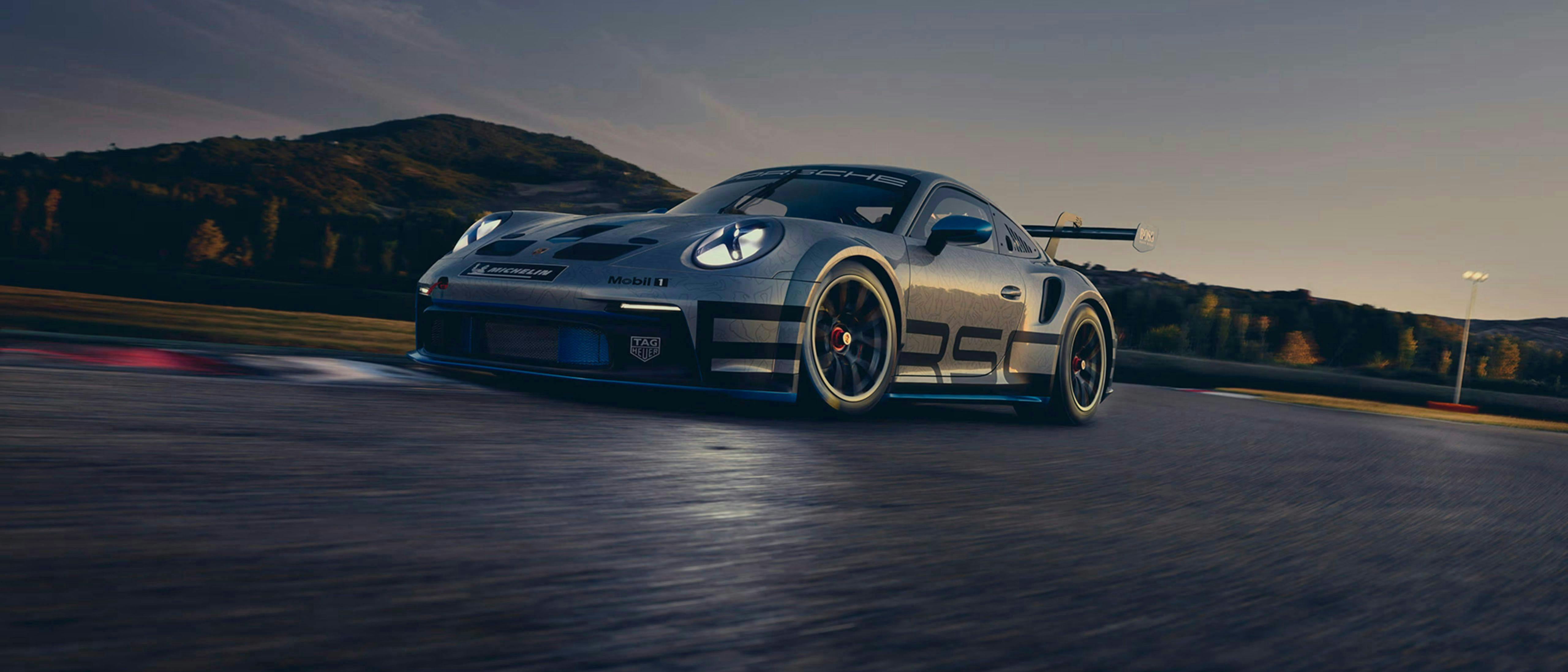 Porsche 911 argentée de la Porsche Carrera Cup Benelux roulant à haute vitesse sur un circuit au coucher du soleil.