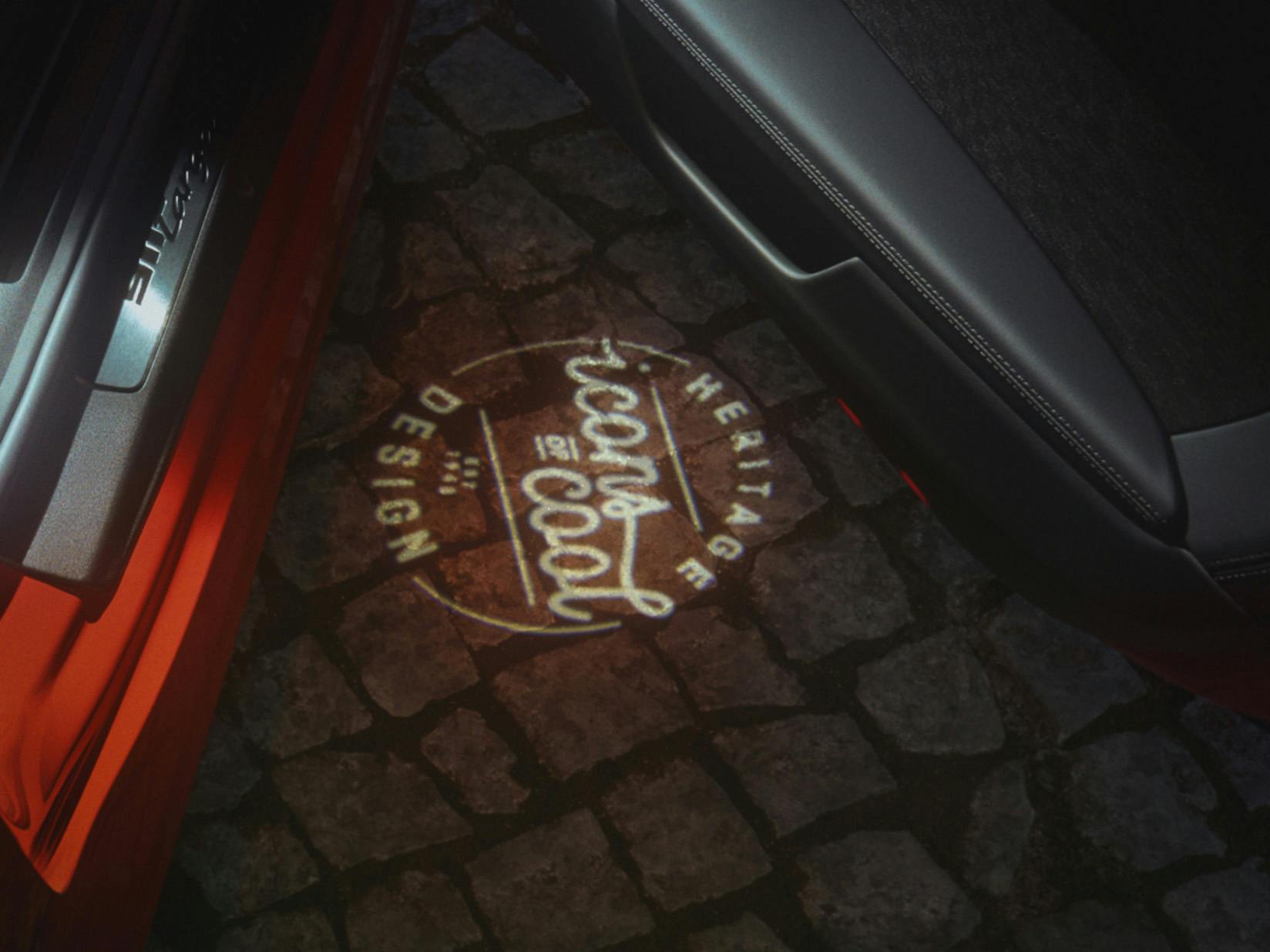 View of the 'Icons of Cool' emblem projection on the floor under the open passenger door of a Porsche.