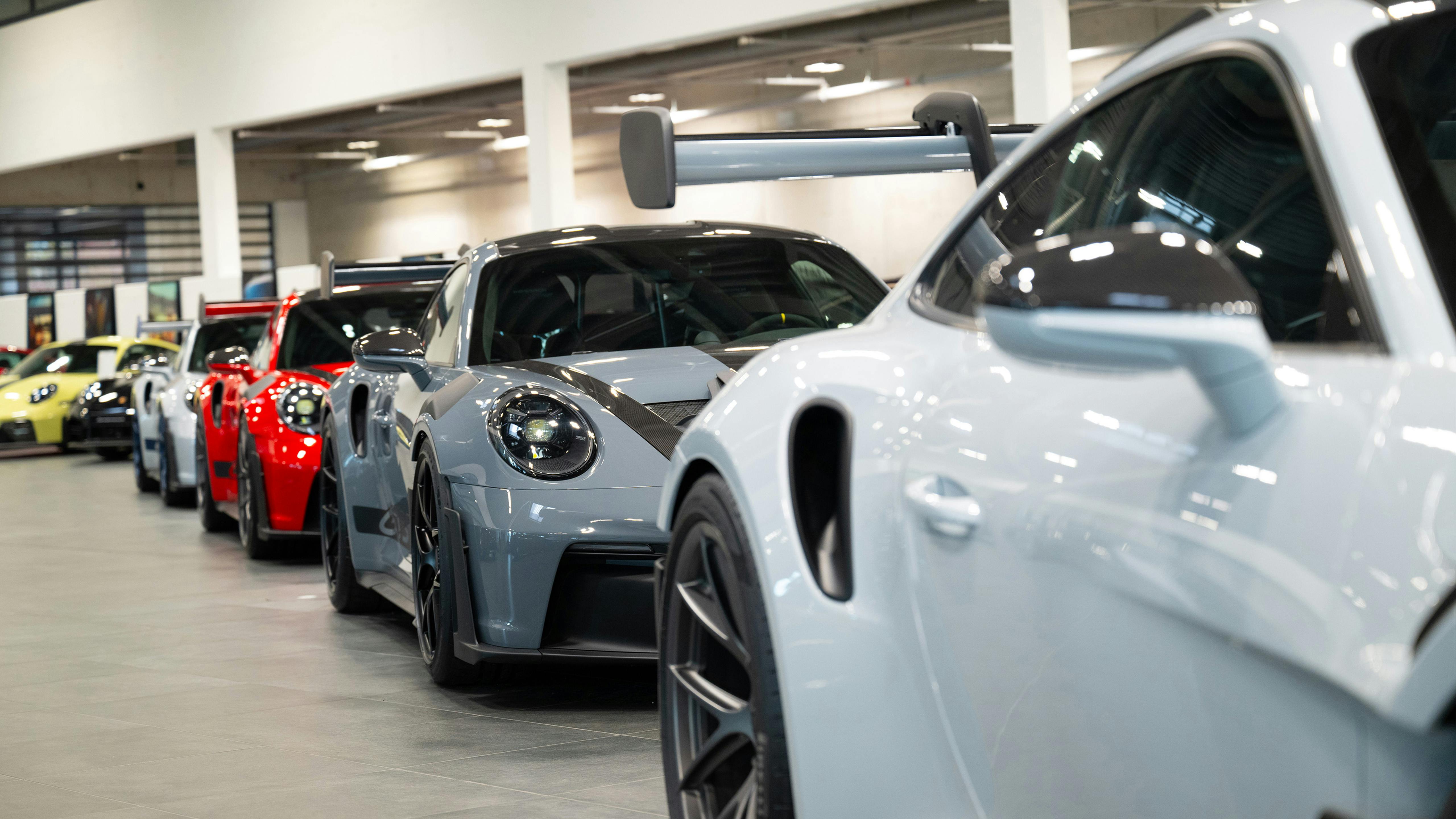 Weißer Porsche mit Heckspoiler im Vordergrund vor grauen, roten und gelben Modellen im Showroom.