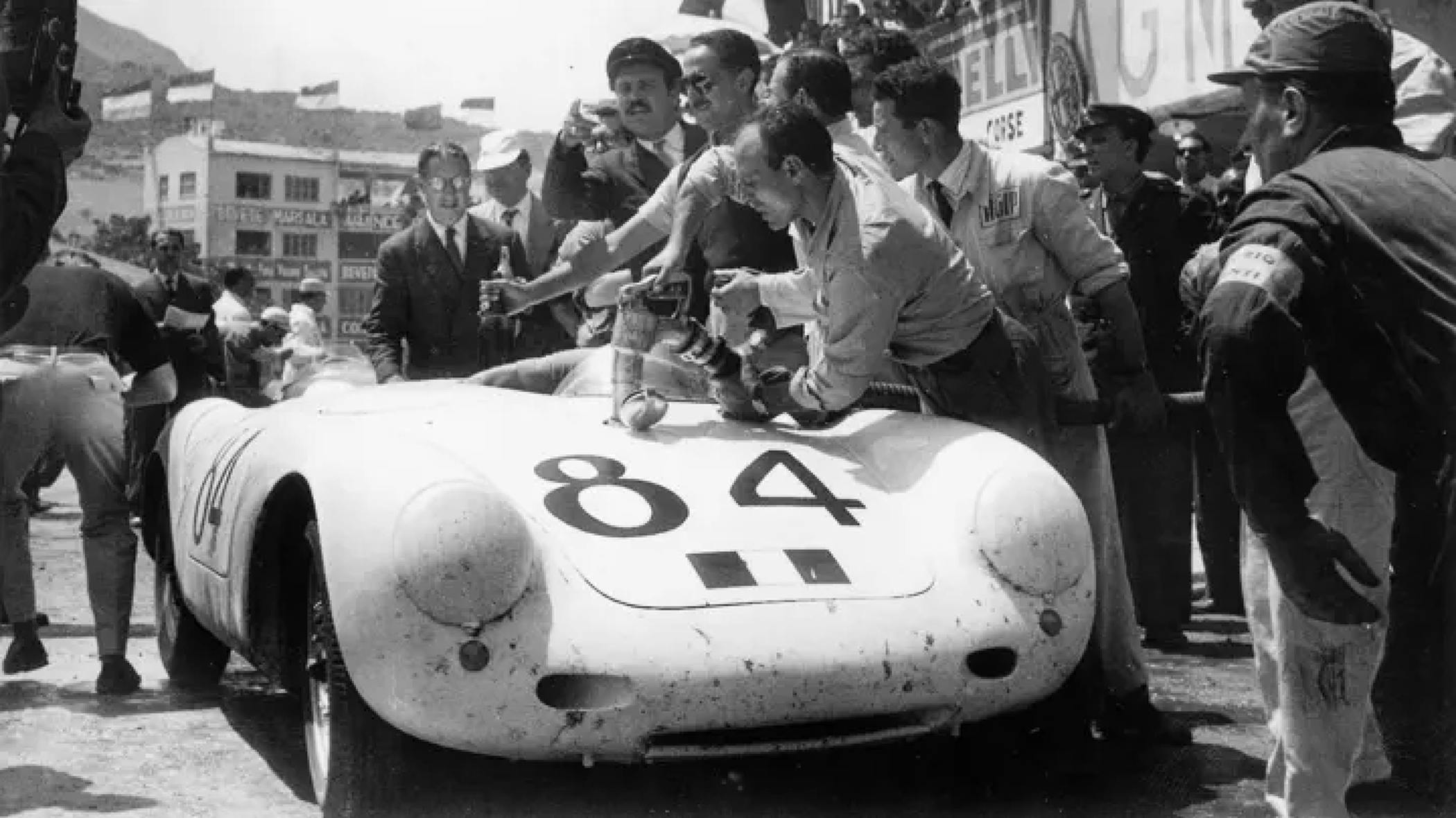 Several people standing around a classic Porsche race car.