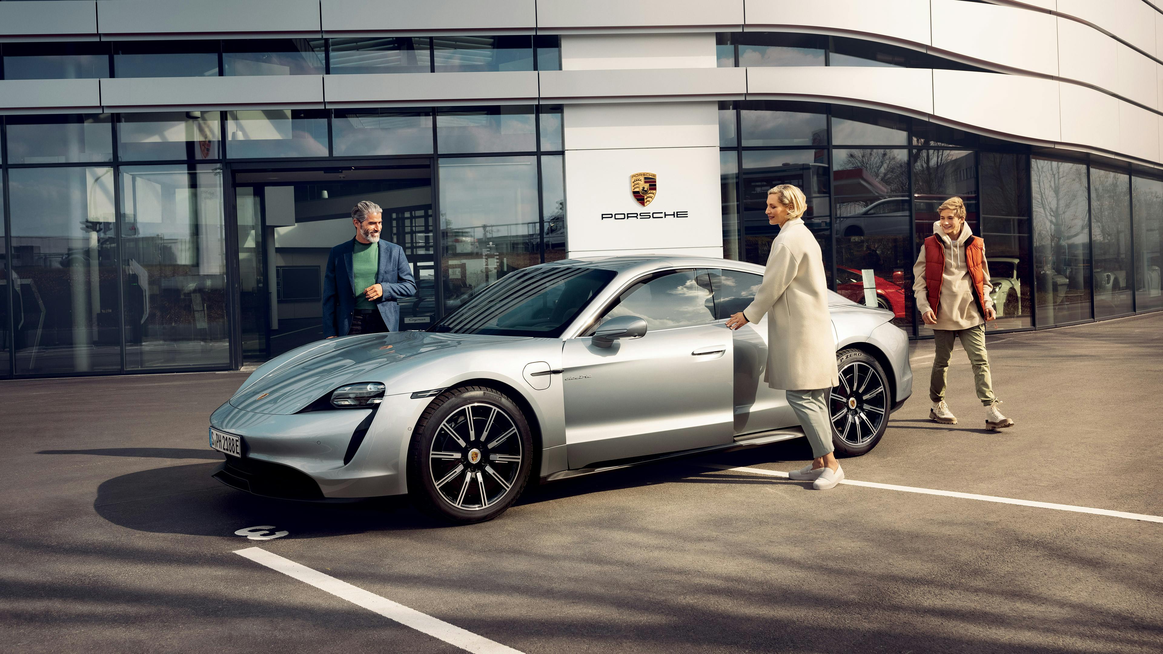 Eine Familie steigt vor einem Porsche Niederlassung in ein Taycan ein.