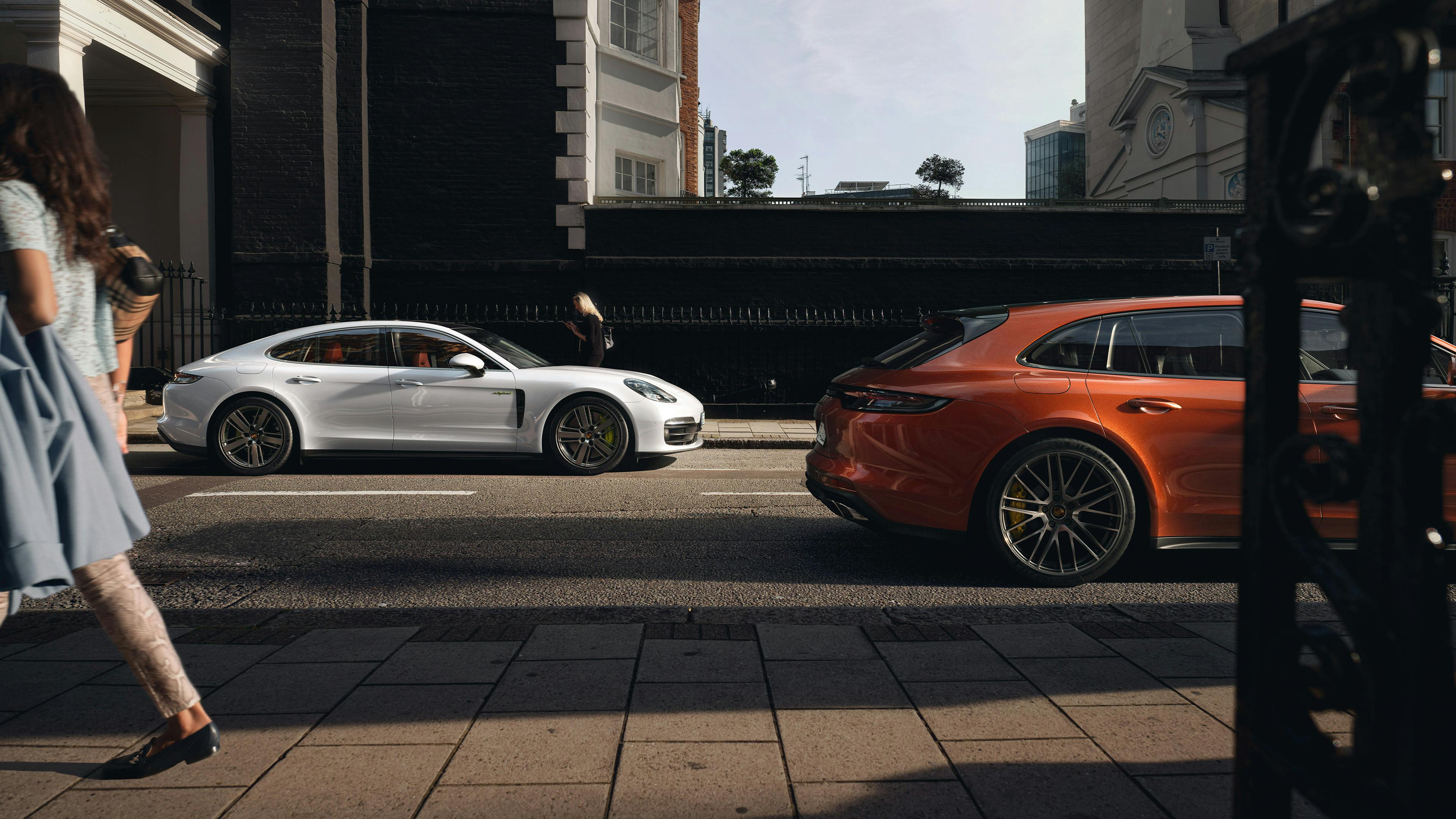 Ein weißer und ein Maderagold-metallic Porsche sind an einer Straße geparkt.