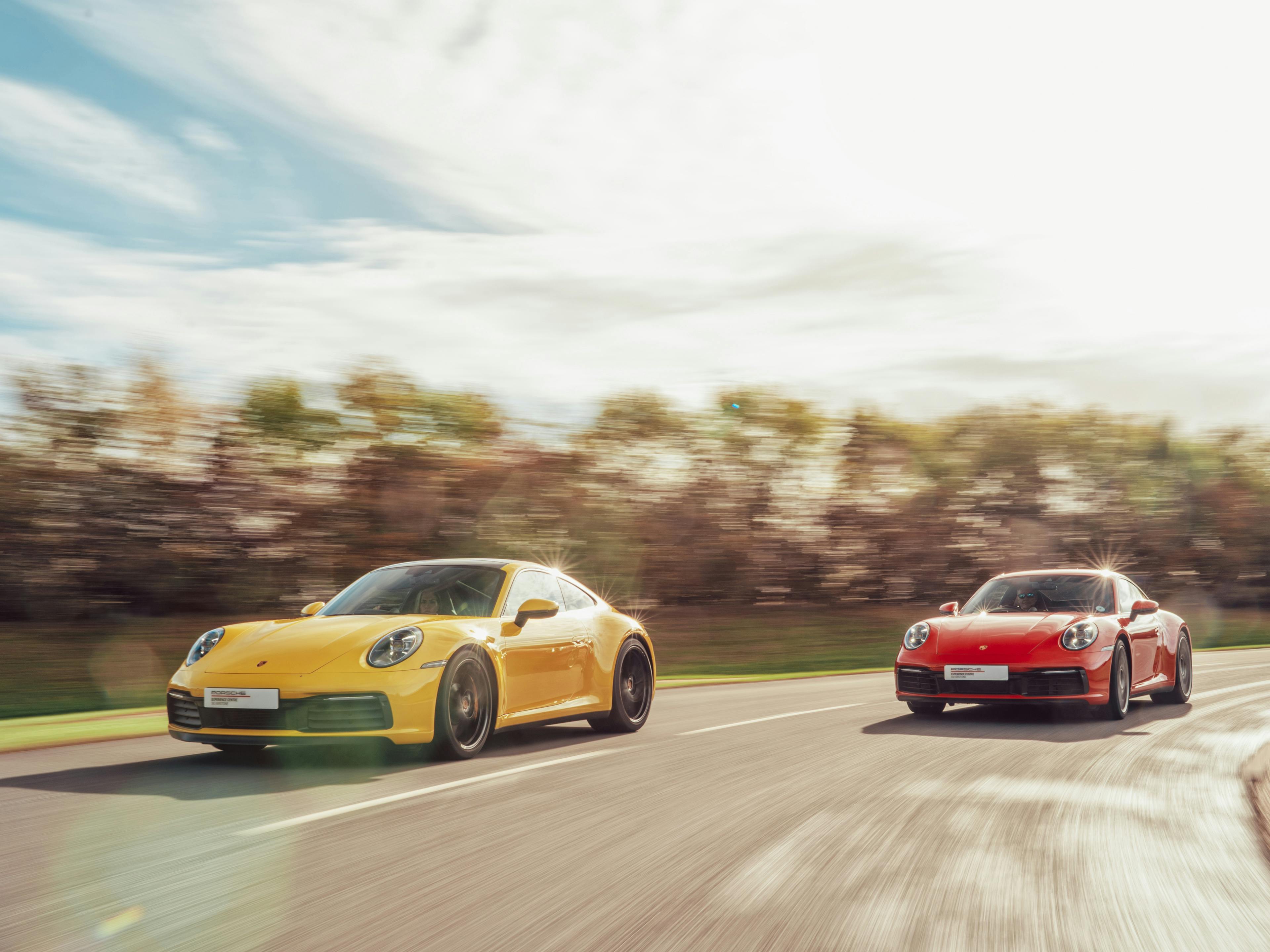 A yellow Porsche 911 Carrera driving on the race track at Porsche Experience Centre Silverstone with a red 911 Carrera close behind.