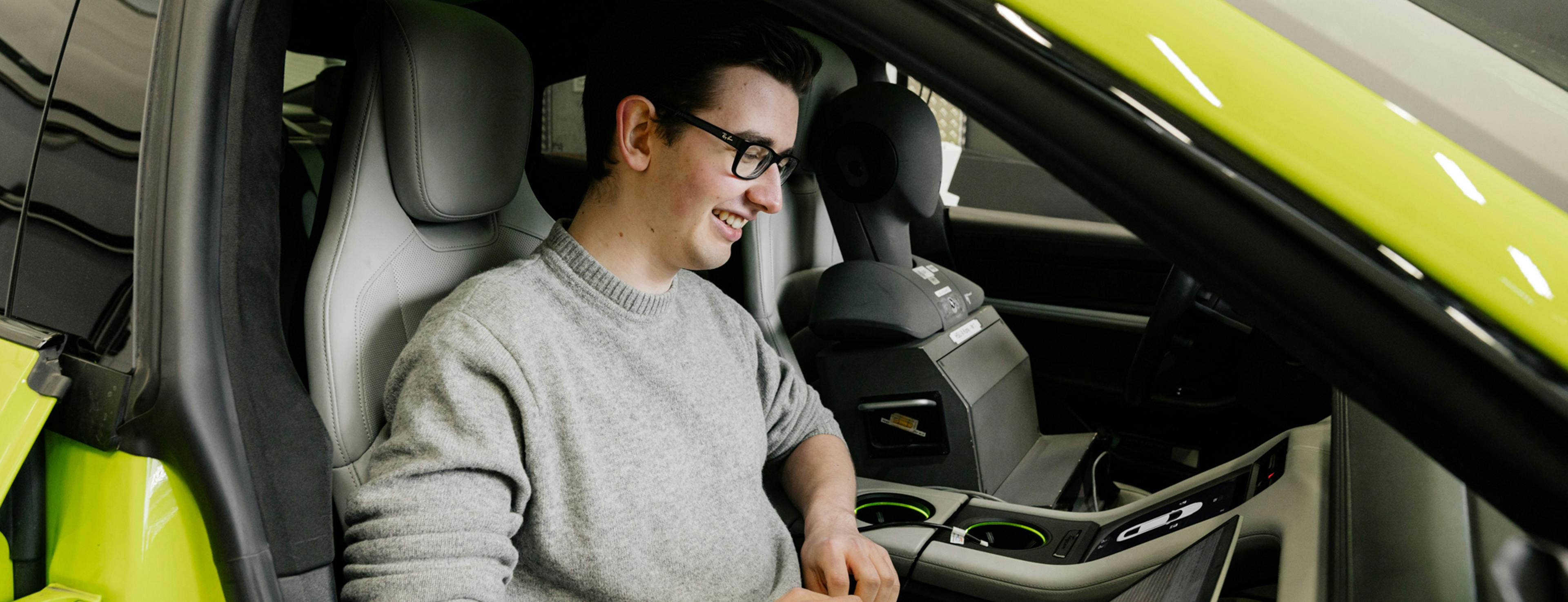 Ein Porsche Mitarbeiter sitzt auf dem Beifahrersitz an einem Prüfstand und arbeitet am Laptop.