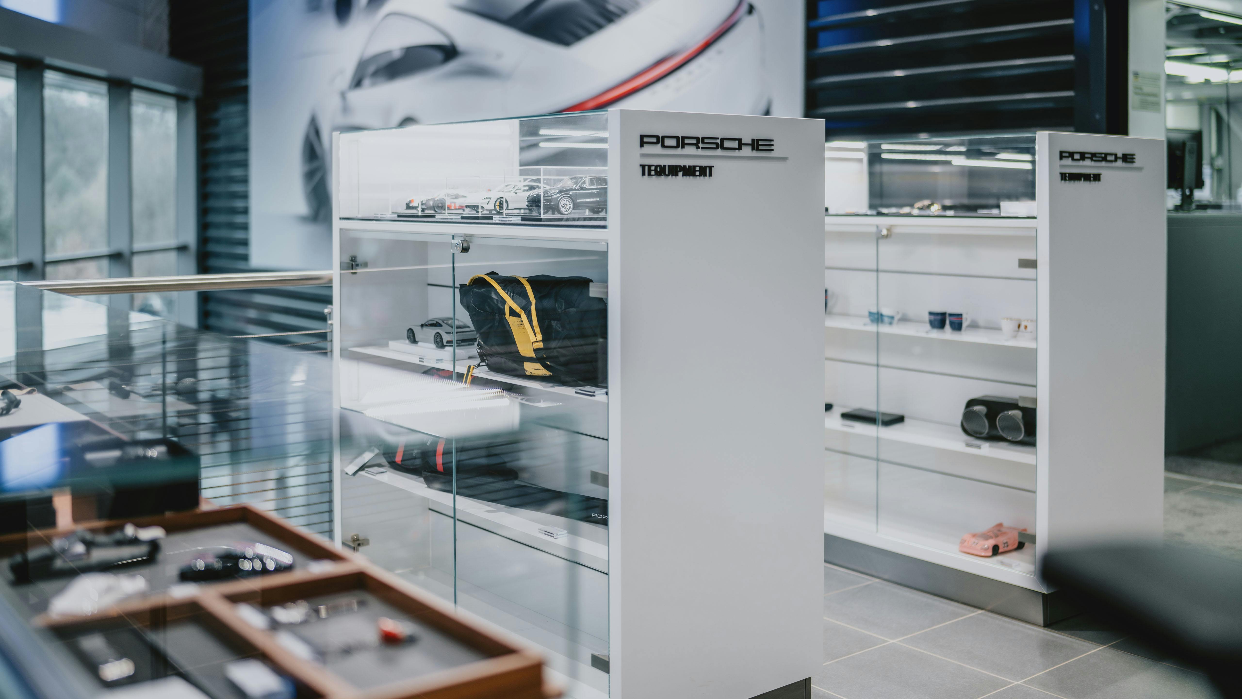 Plusieurs produits Porsche Tequipment exposés dans deux vitrines blanches et en verre au dernier étage du Porsche Zenter Lëtzebuerg.