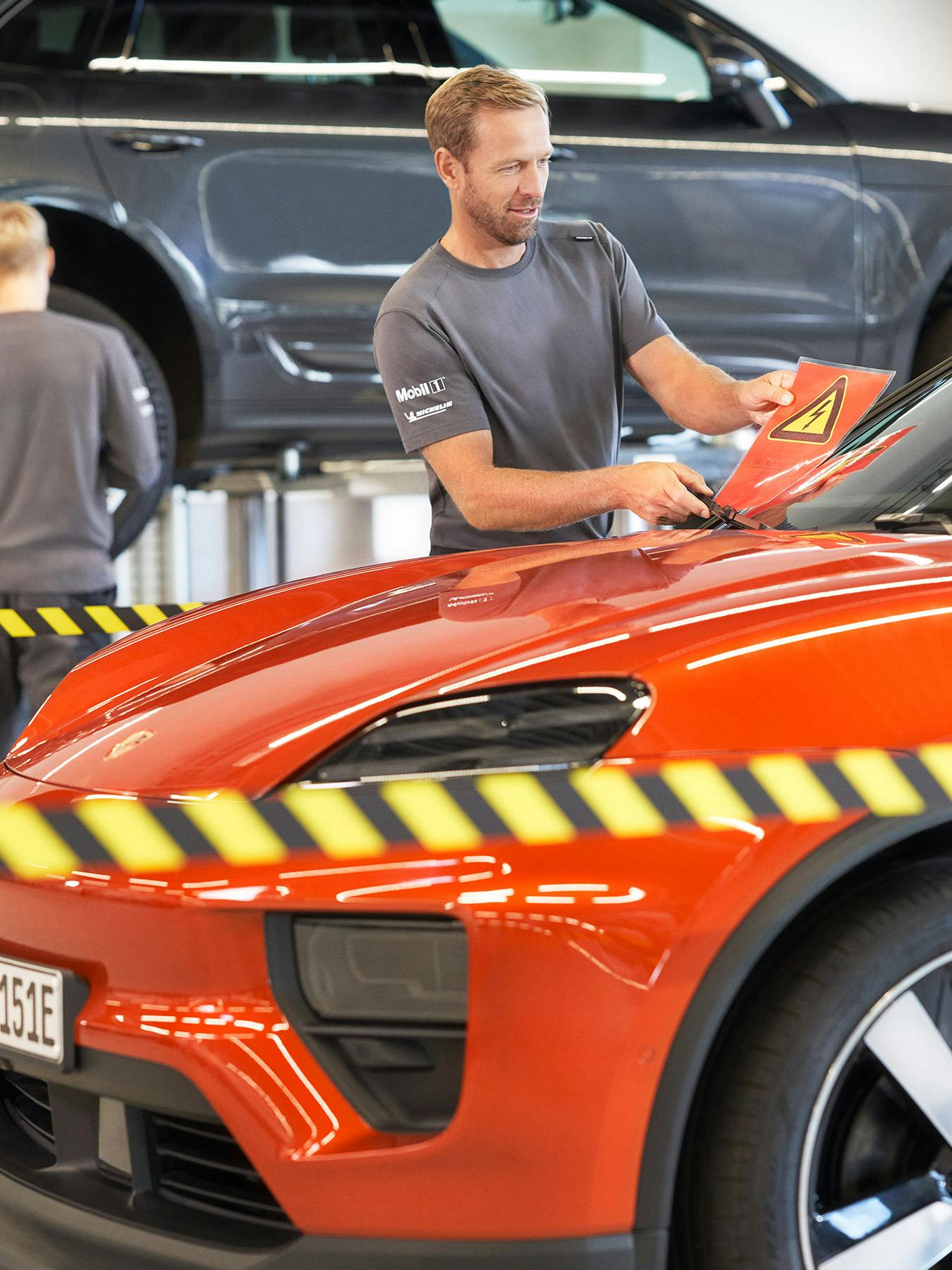 Un technicien travaillant sur un Porsche Macan orange dans un atelier.