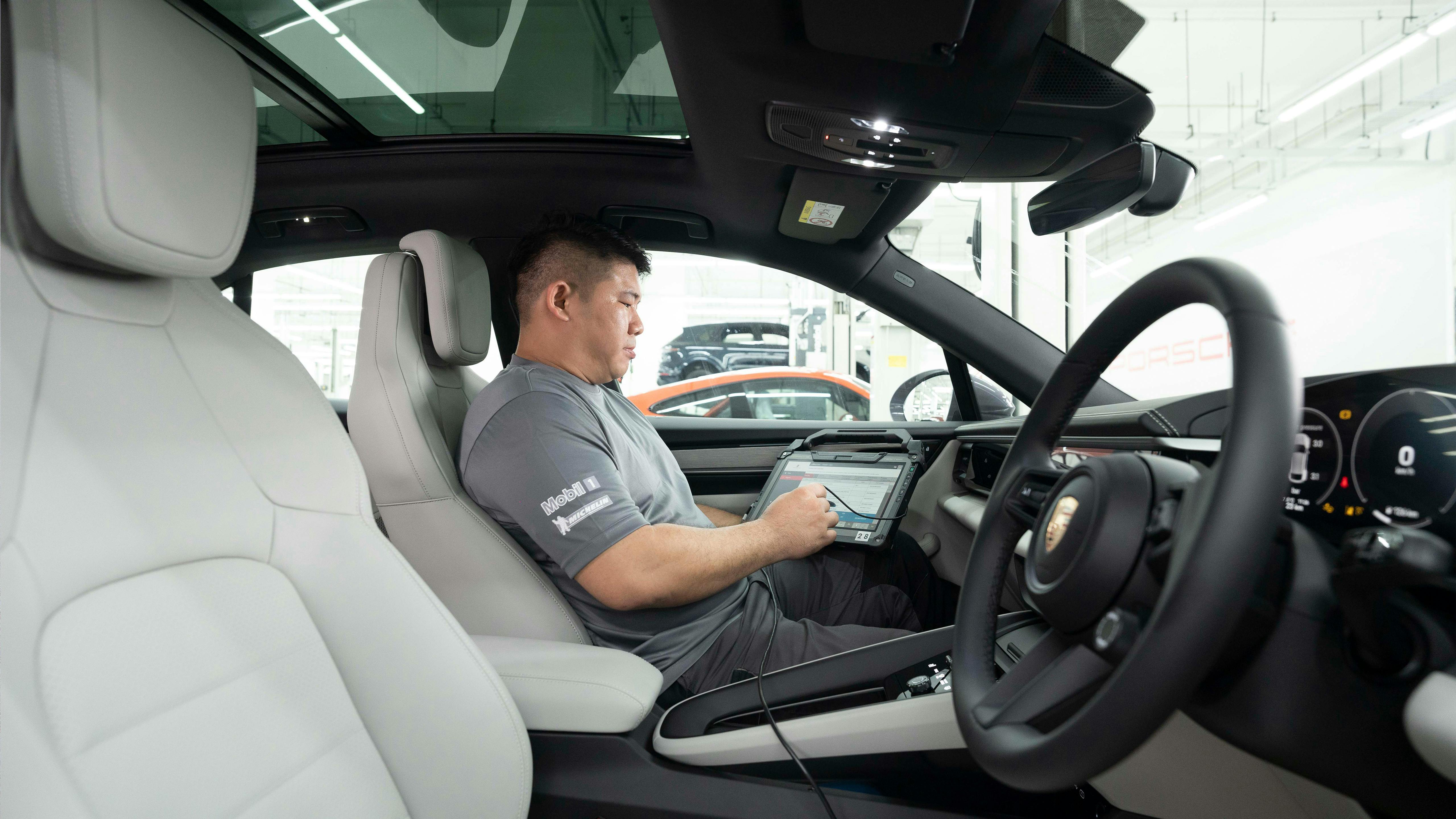 Porsche technician seated in the car using a diagnostic tablet to check the vehicle’s interior systems.