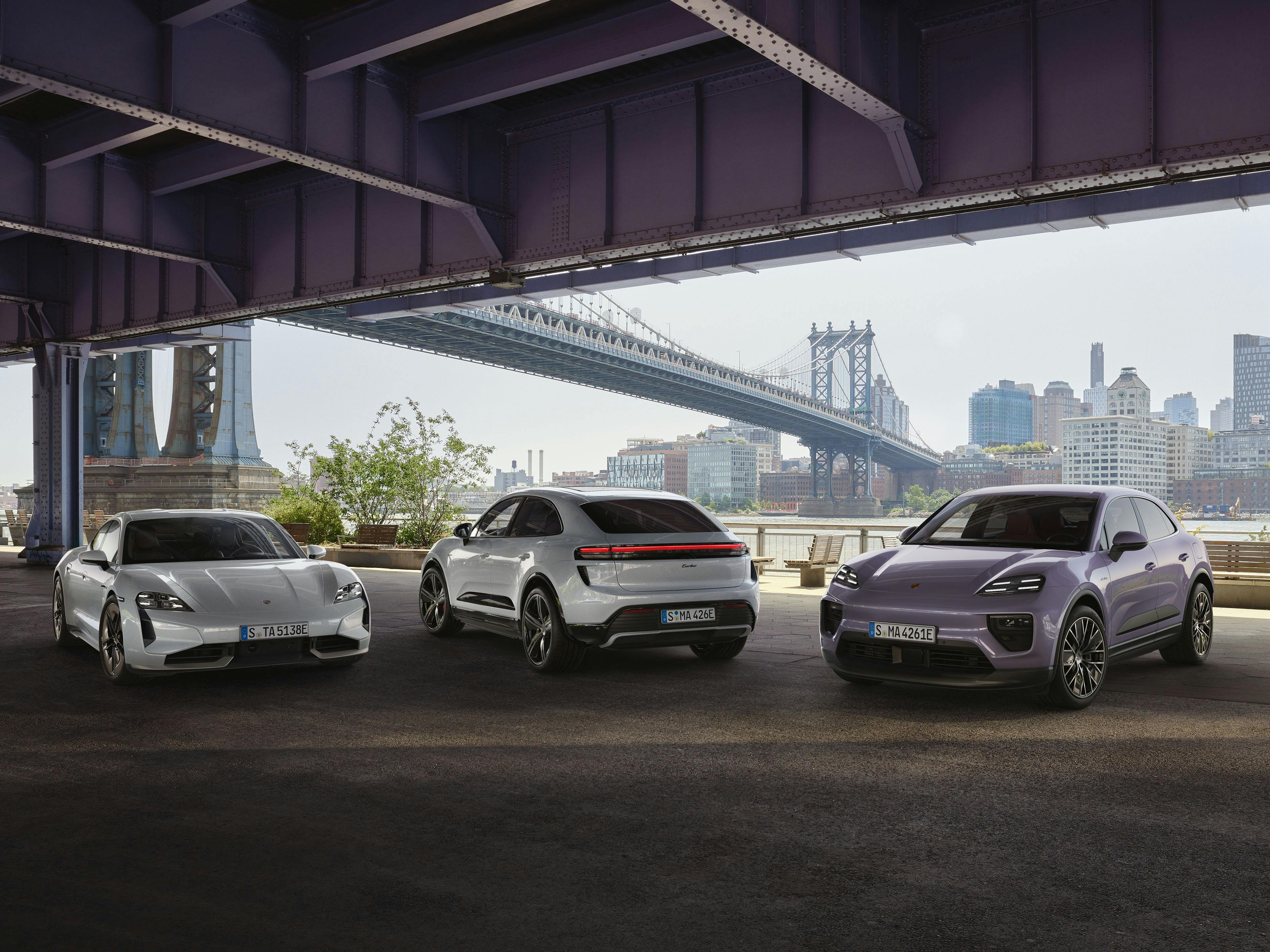 Three electric Porsche vehicles underneath a bridge with a city in the backdrop.
