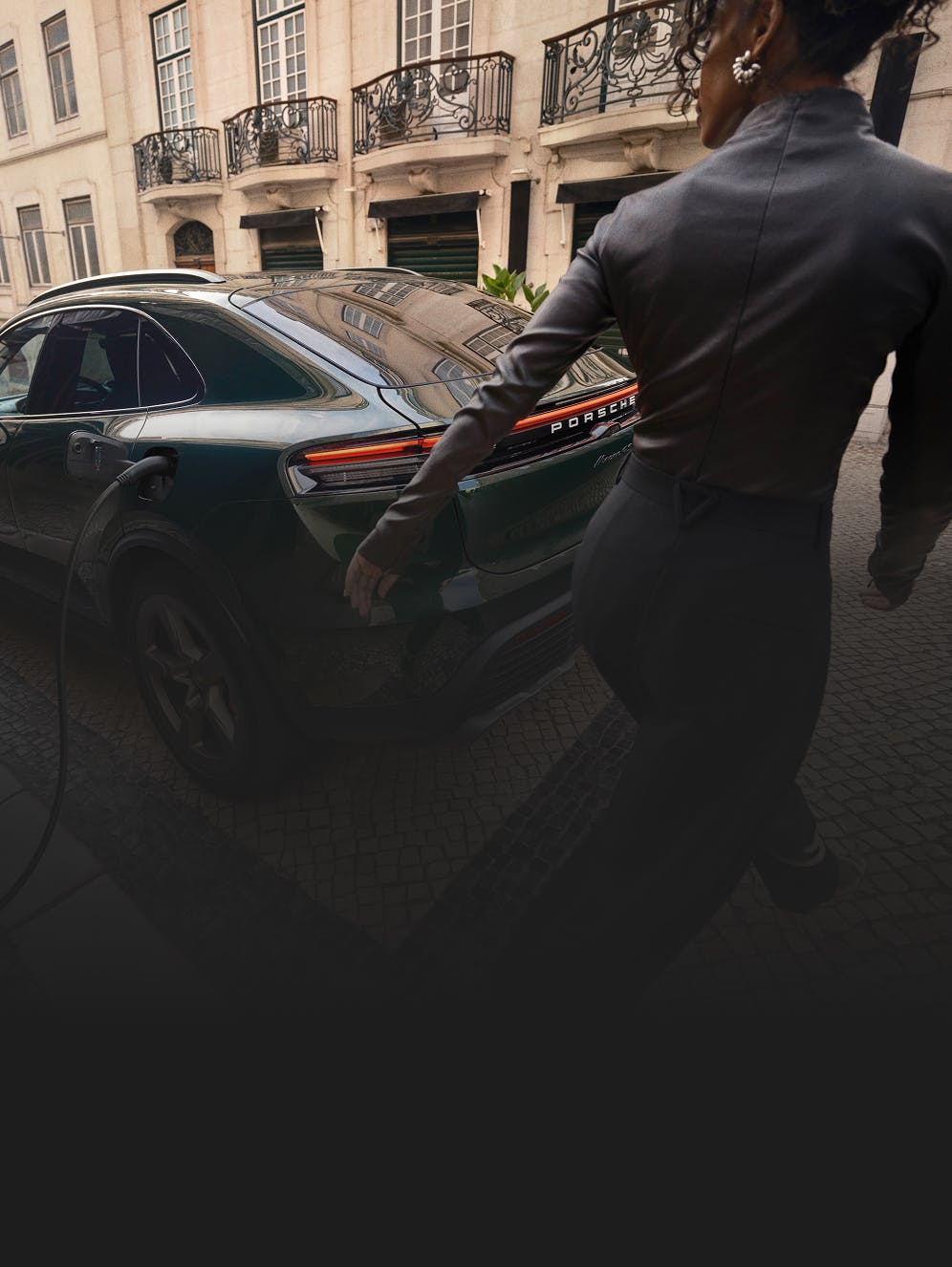 A woman walking past a Porsche Macan 4 at a charger.