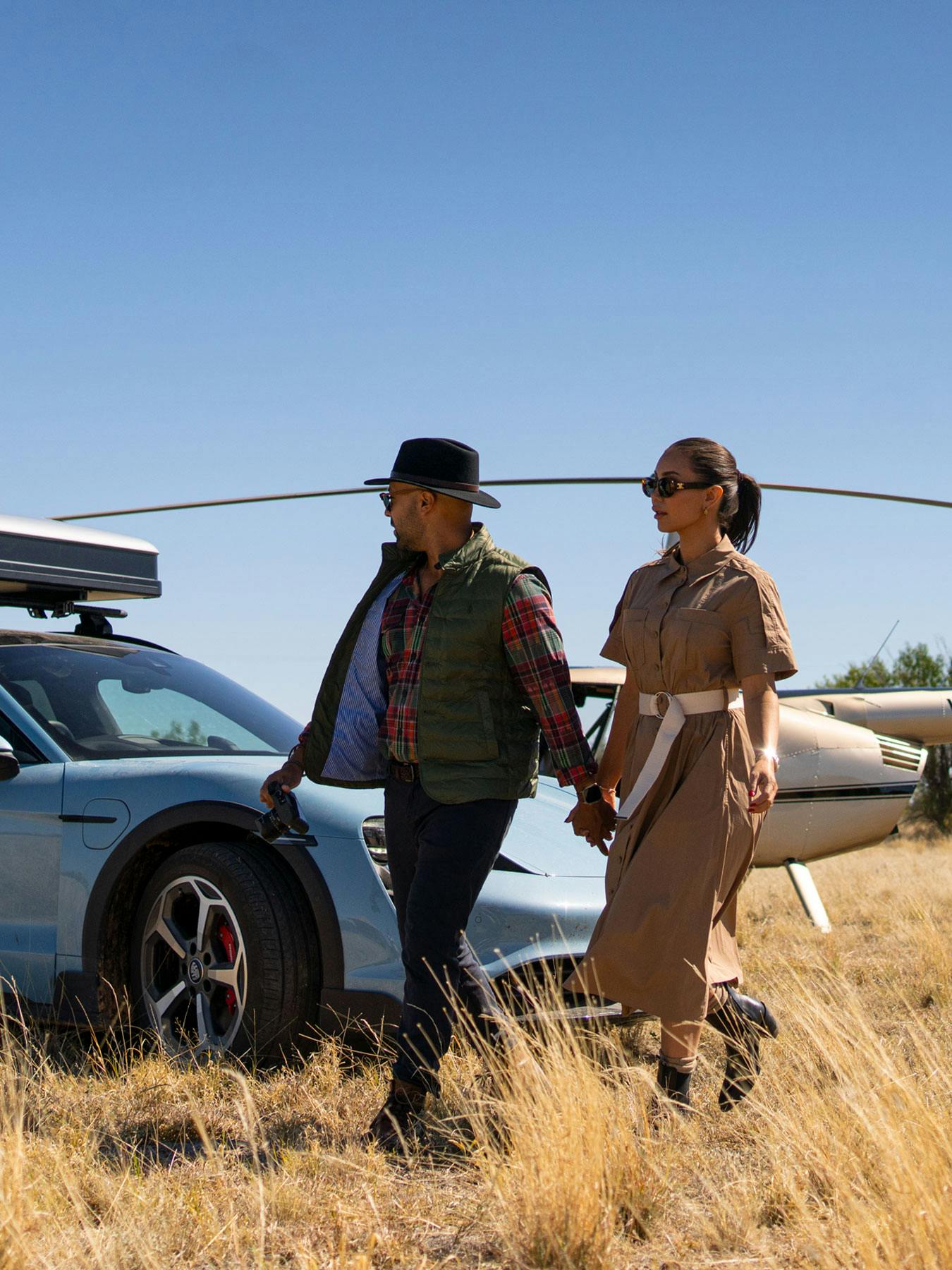 A male and female walking walk porsche taycan with helicopter behind