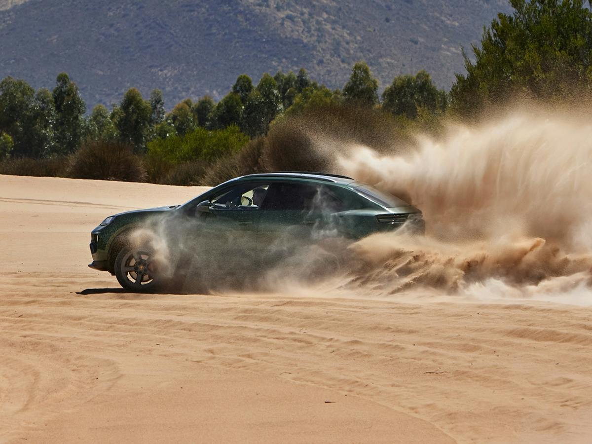 Um Porsche Macan 4S a circular sobre areia e a levantar poeira. A floresta e as montanhas estão em segundo plano.