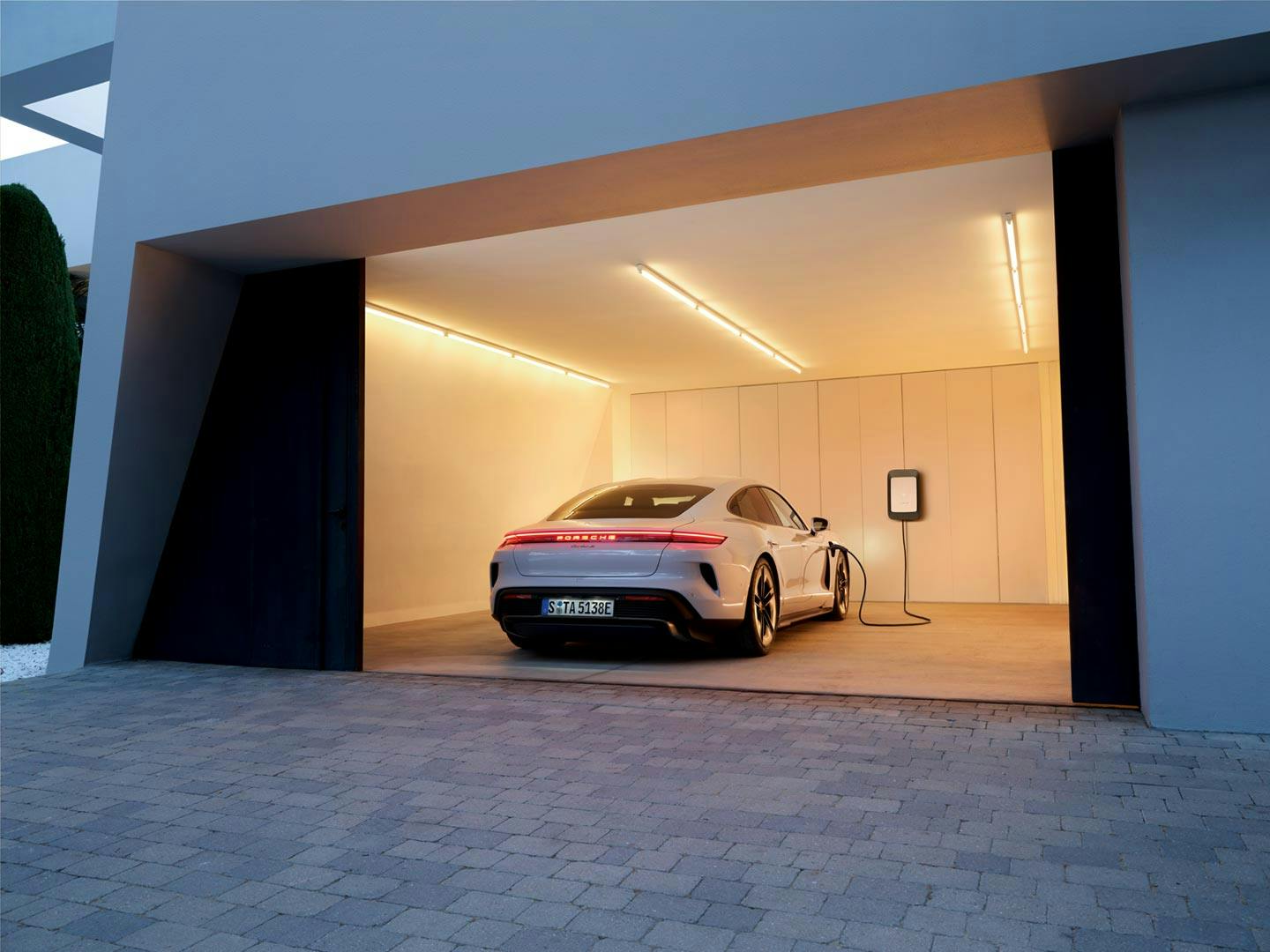 En vit Porsche Taycan Turbo S står på laddning vid en wallbox i ett garage.