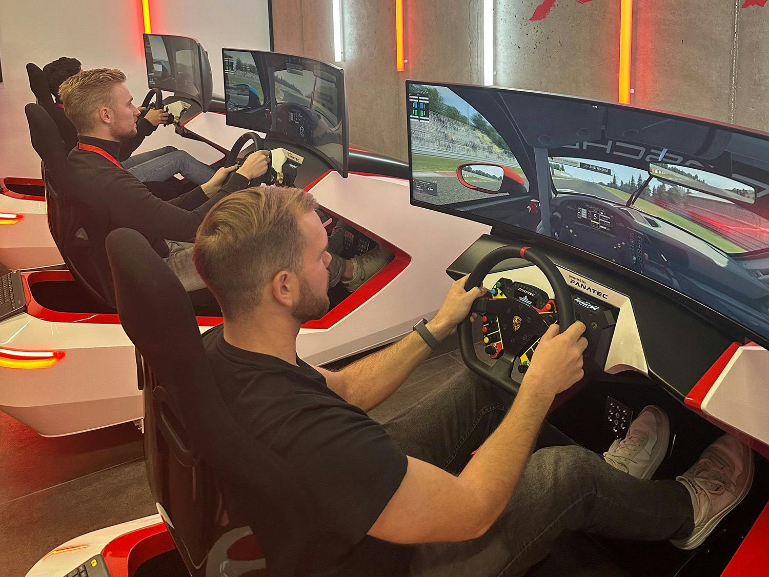 Drei junge Männer sitzen am Porsche Racing Simulator.