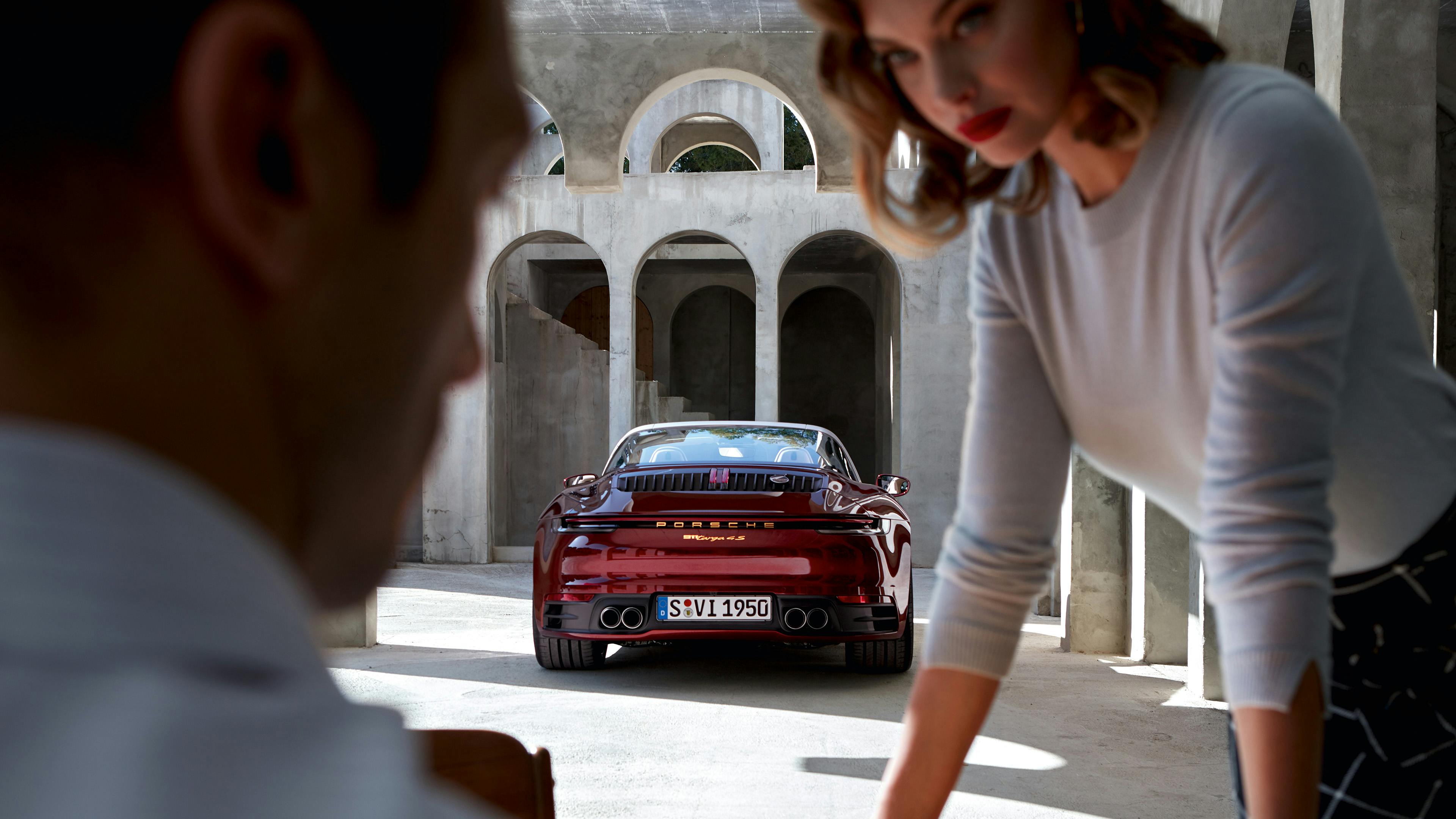 911 Targa 4S Heritage Design Edition stands in front of a historic building with arches, two people discussing something in the foreground.