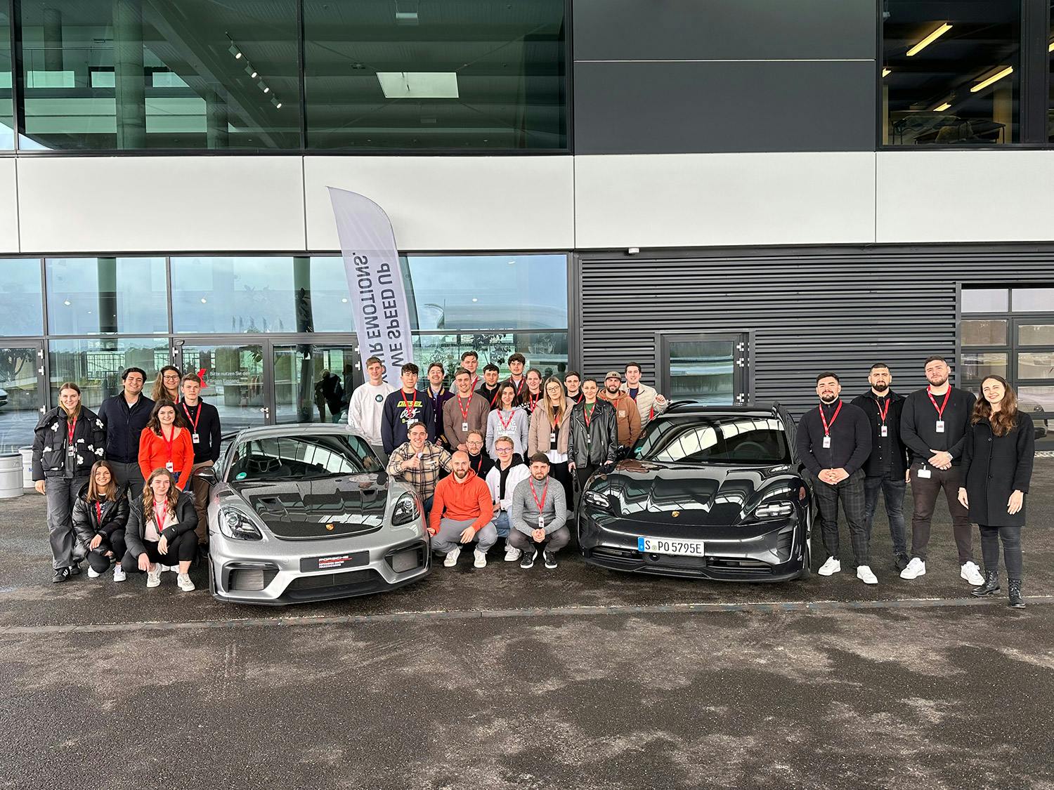 Eine Gruppe von jungen Menschen versammelt sich um zwei Porsche Rennwagen.