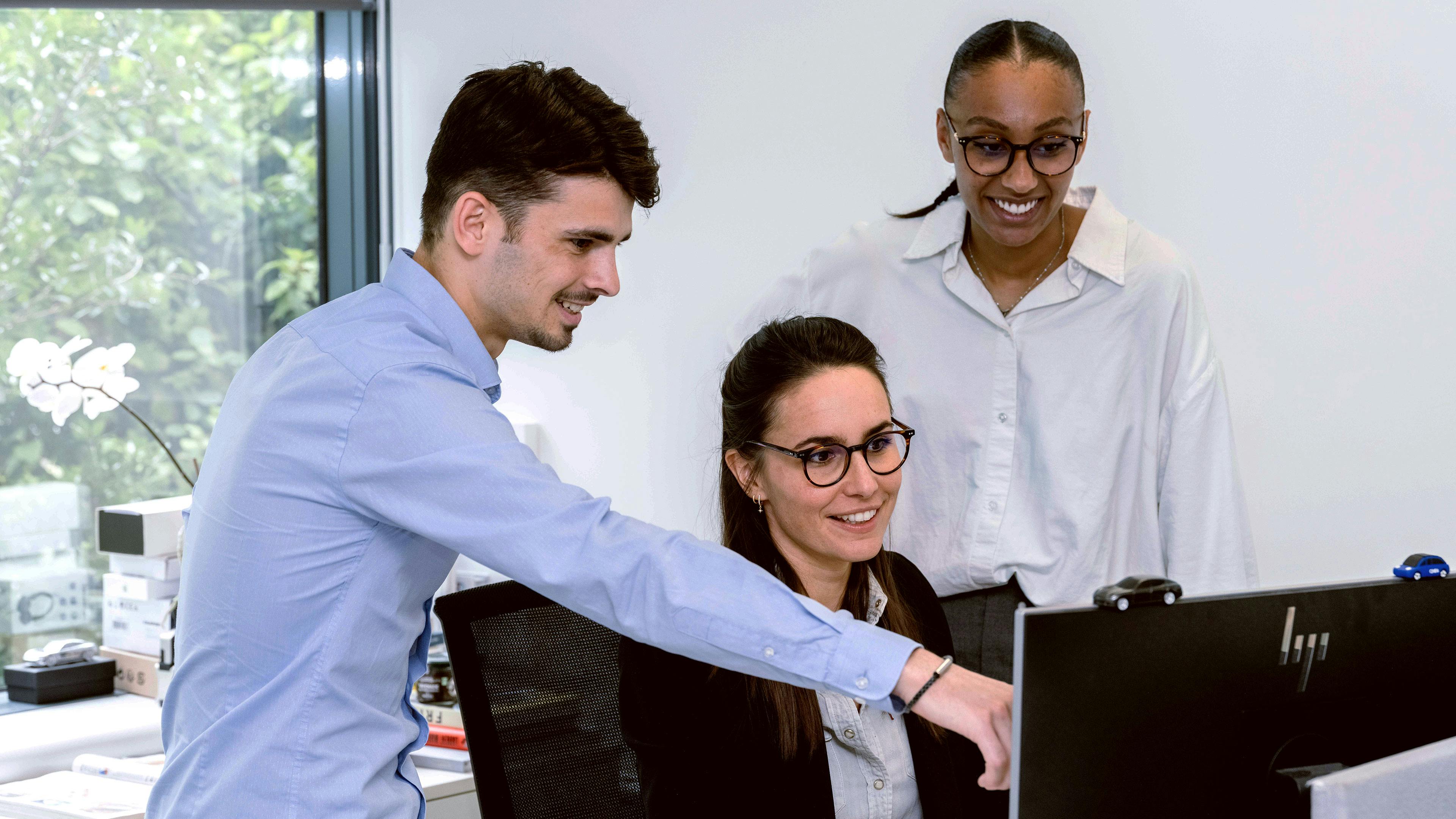 3 people smiling and watching something on a computer.