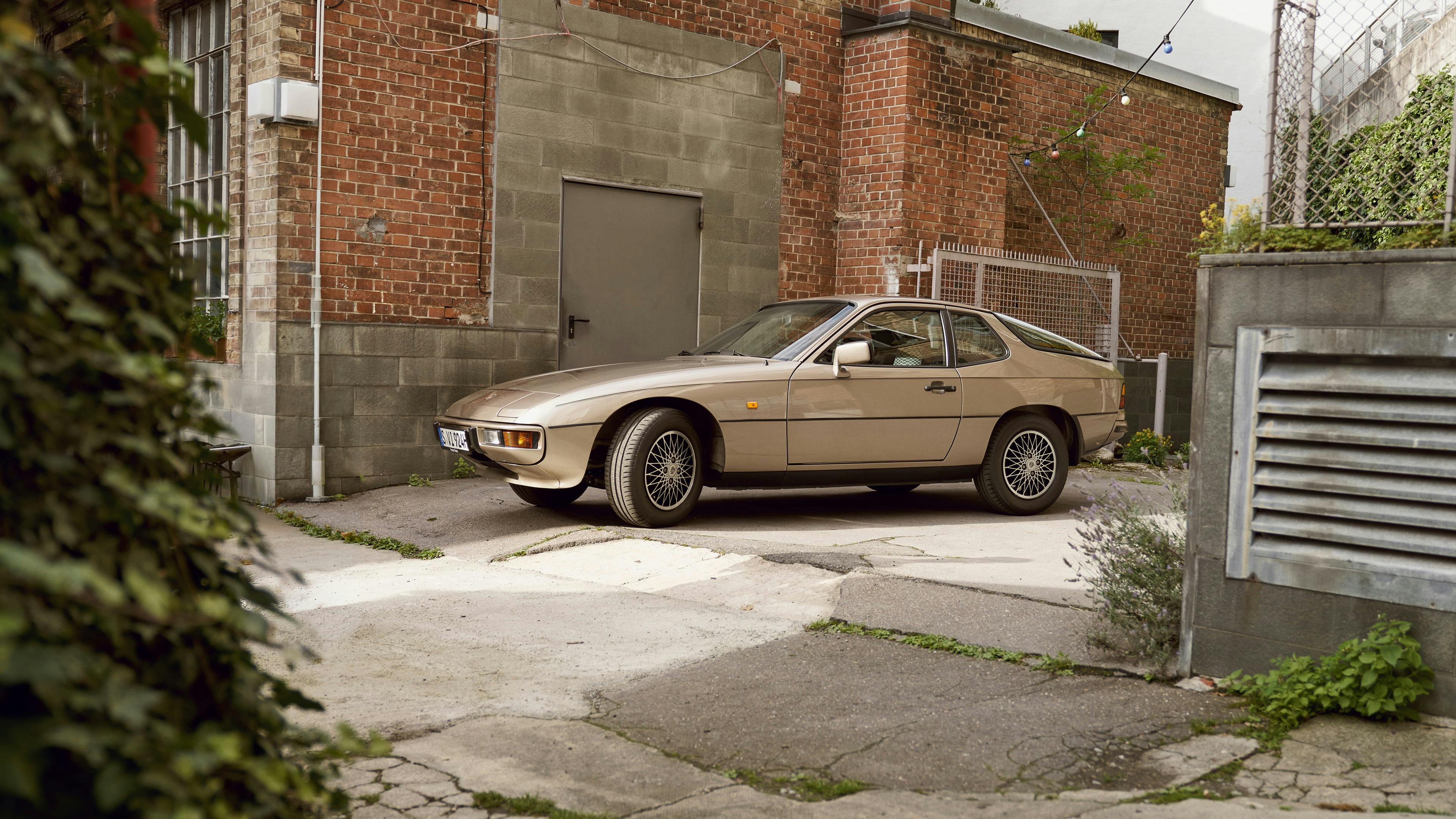 Beige classic Porsche parked beside a brick industrial building in a quiet urban courtyard.