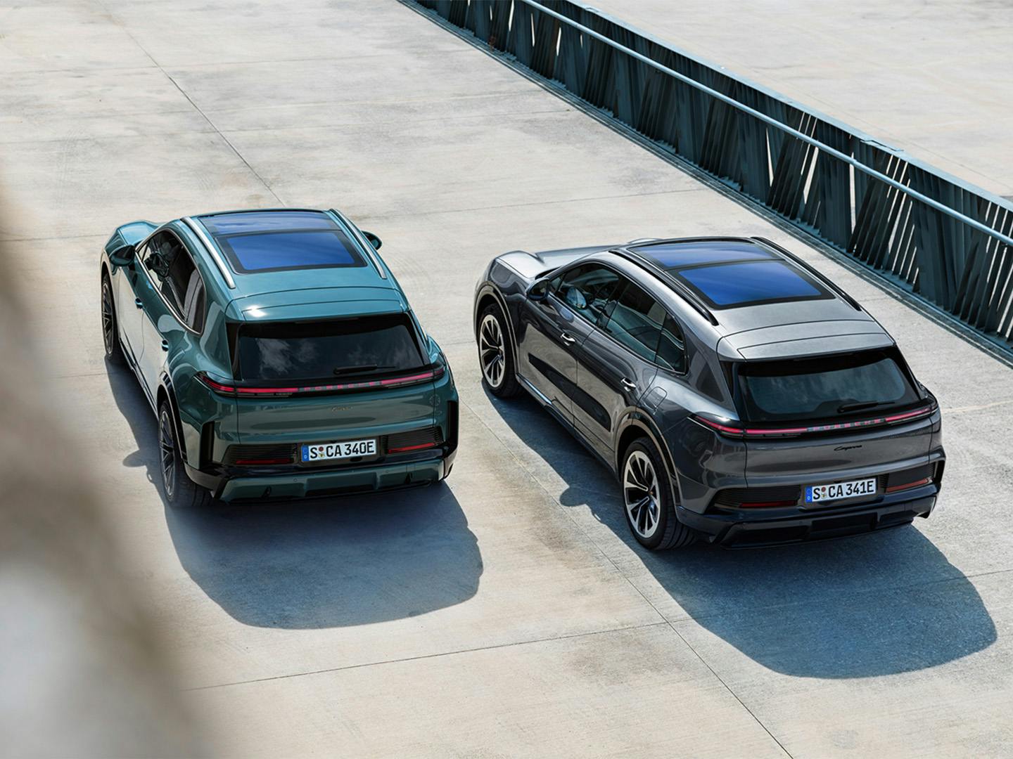 Εναέρια λήψη δύο Porsche Cayenne Electric (Turbo αριστερά, βασική δεξιά) παρκαρισμένων παράλληλα, με πανοραμικές οροφές και ενιαία πίσω φωτεινή λωρίδα.