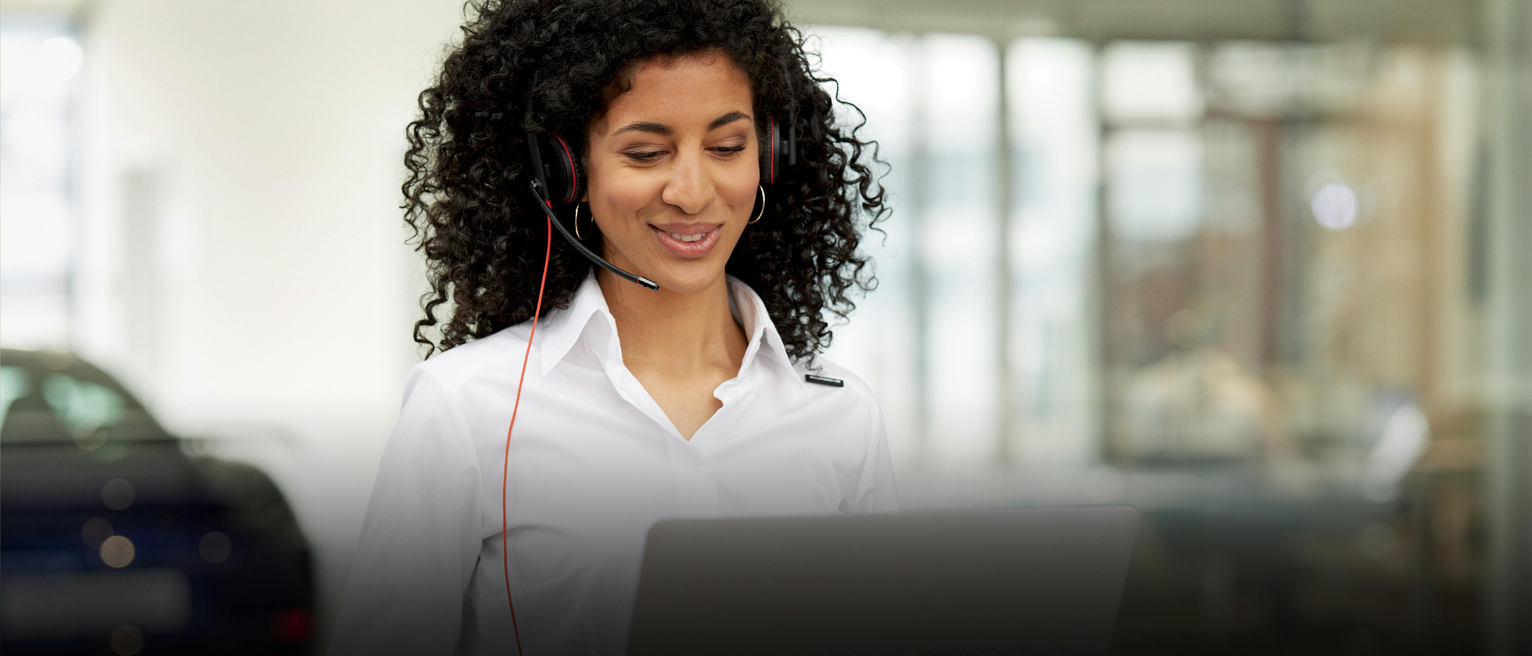 A Porsche service assistant is in a conversation via headphones and looking at her laptop.