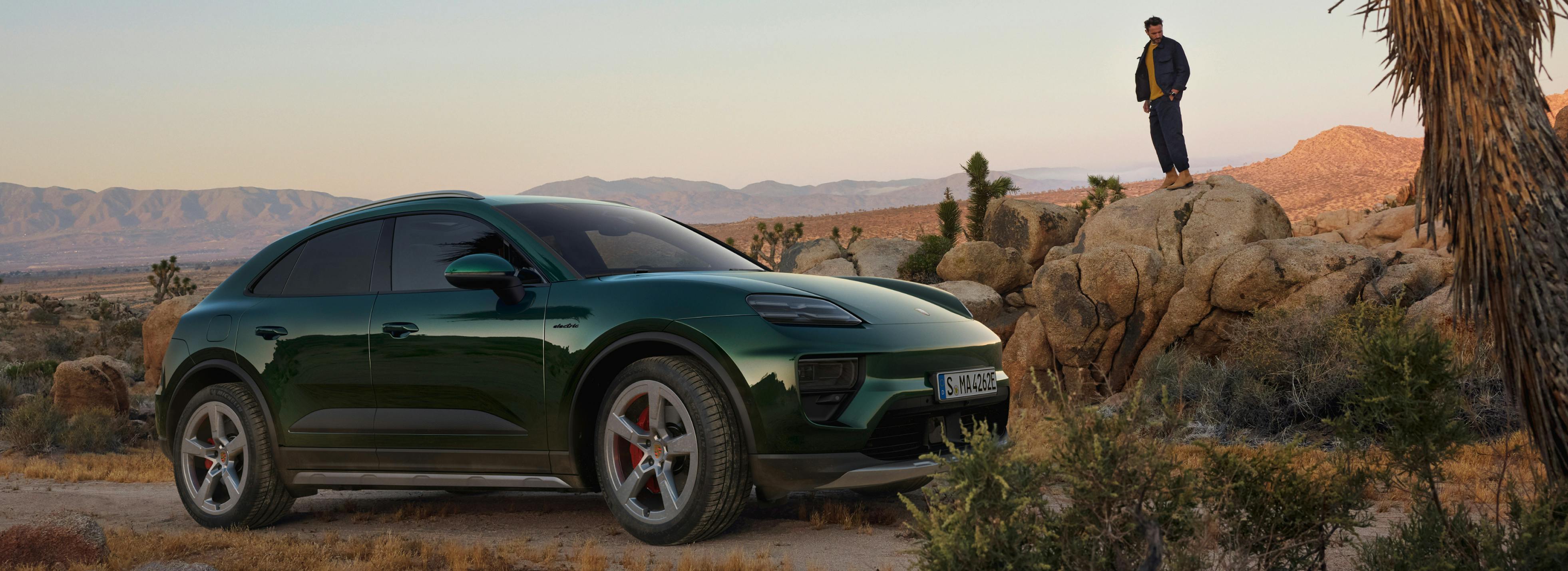 Um Porsche Macan 4S num ambiente desértico com montanhas. Um homem está de pé numa rocha junto ao veículo ao fundo.