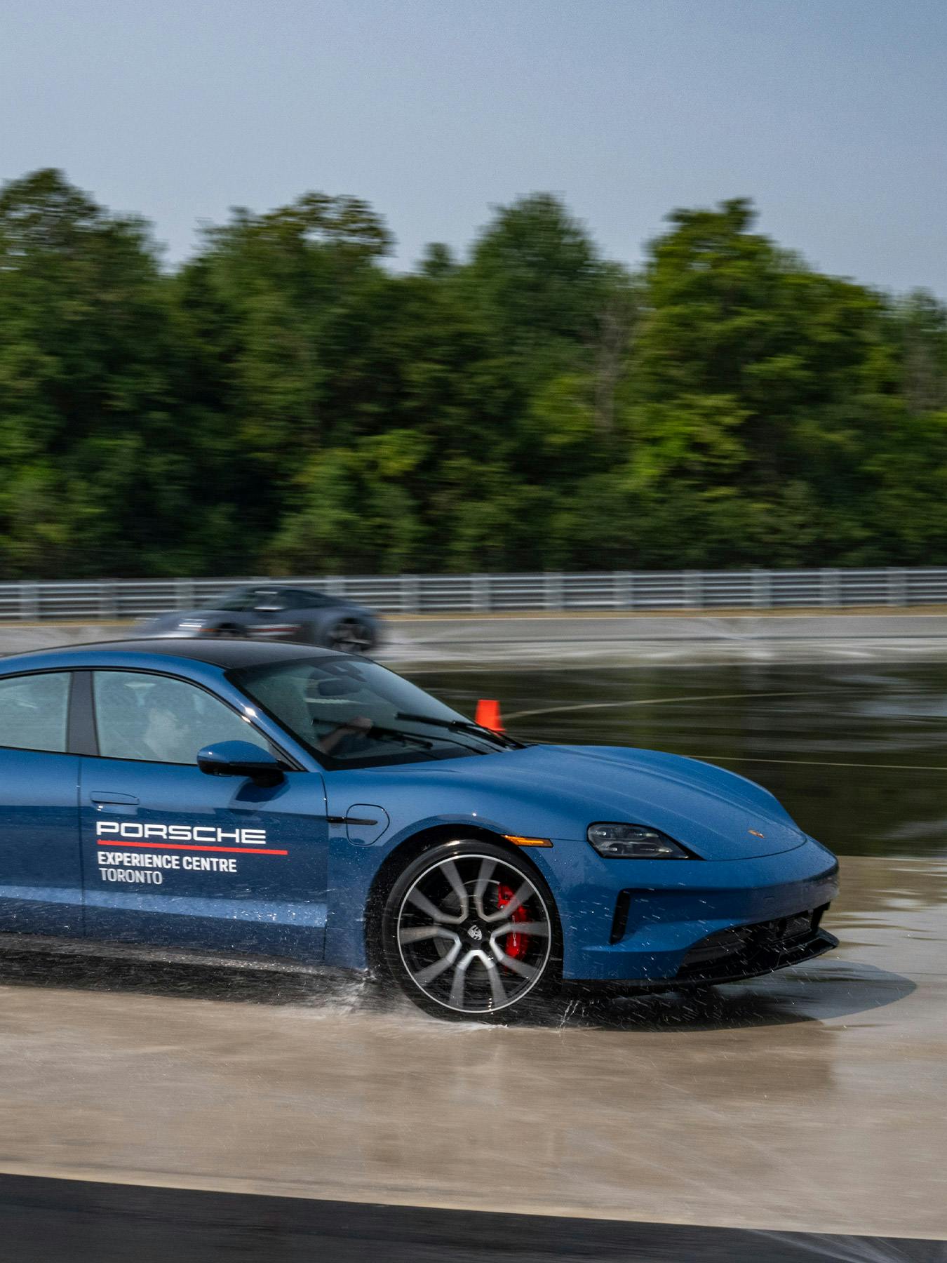 Une Porsche Taycan bleue en mouvement sur un cercle de béton mouillé.